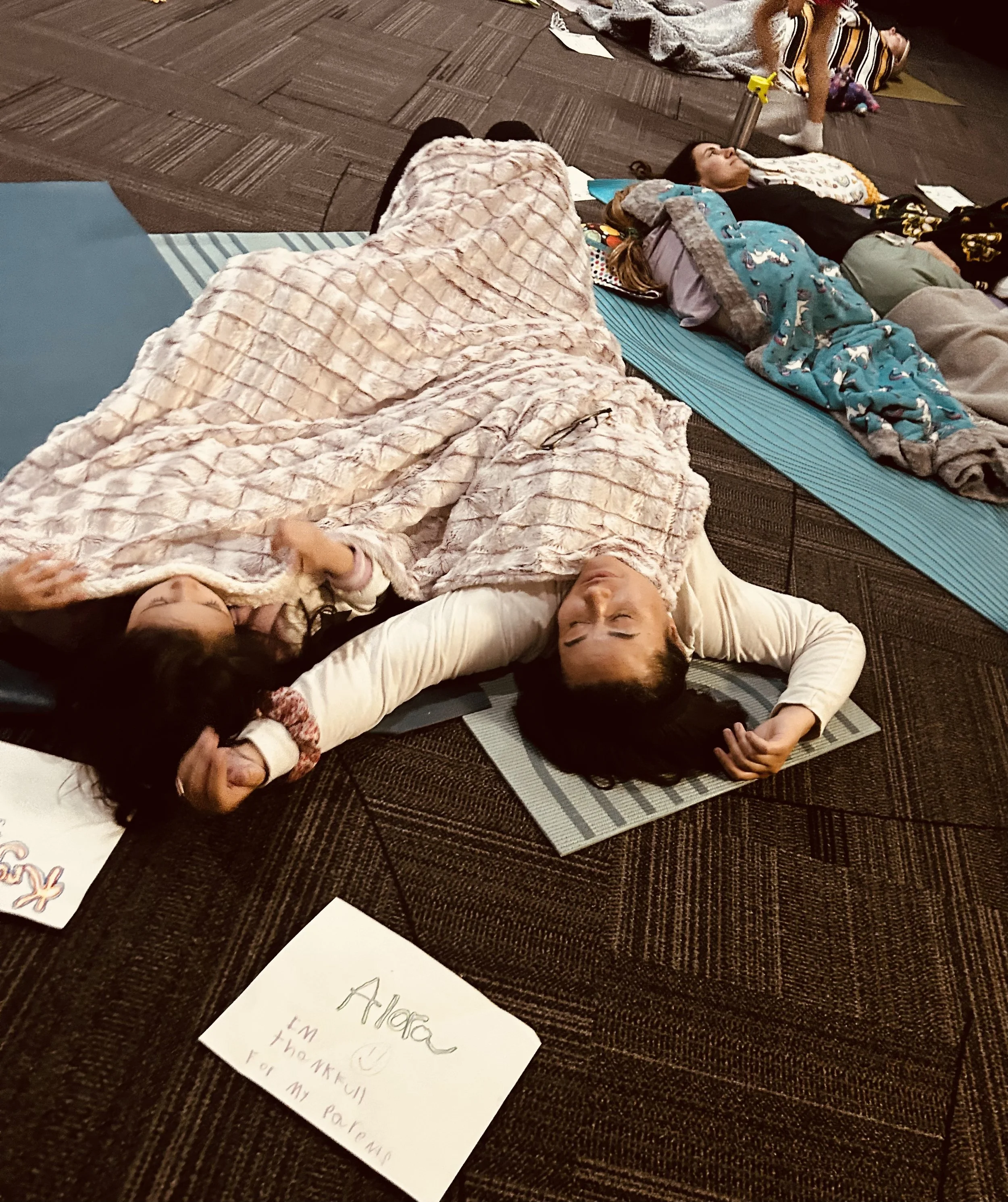 People lying on yoga mats on a carpeted floor, possibly resting or sleeping, with handwritten notes and drawings on paper nearby.