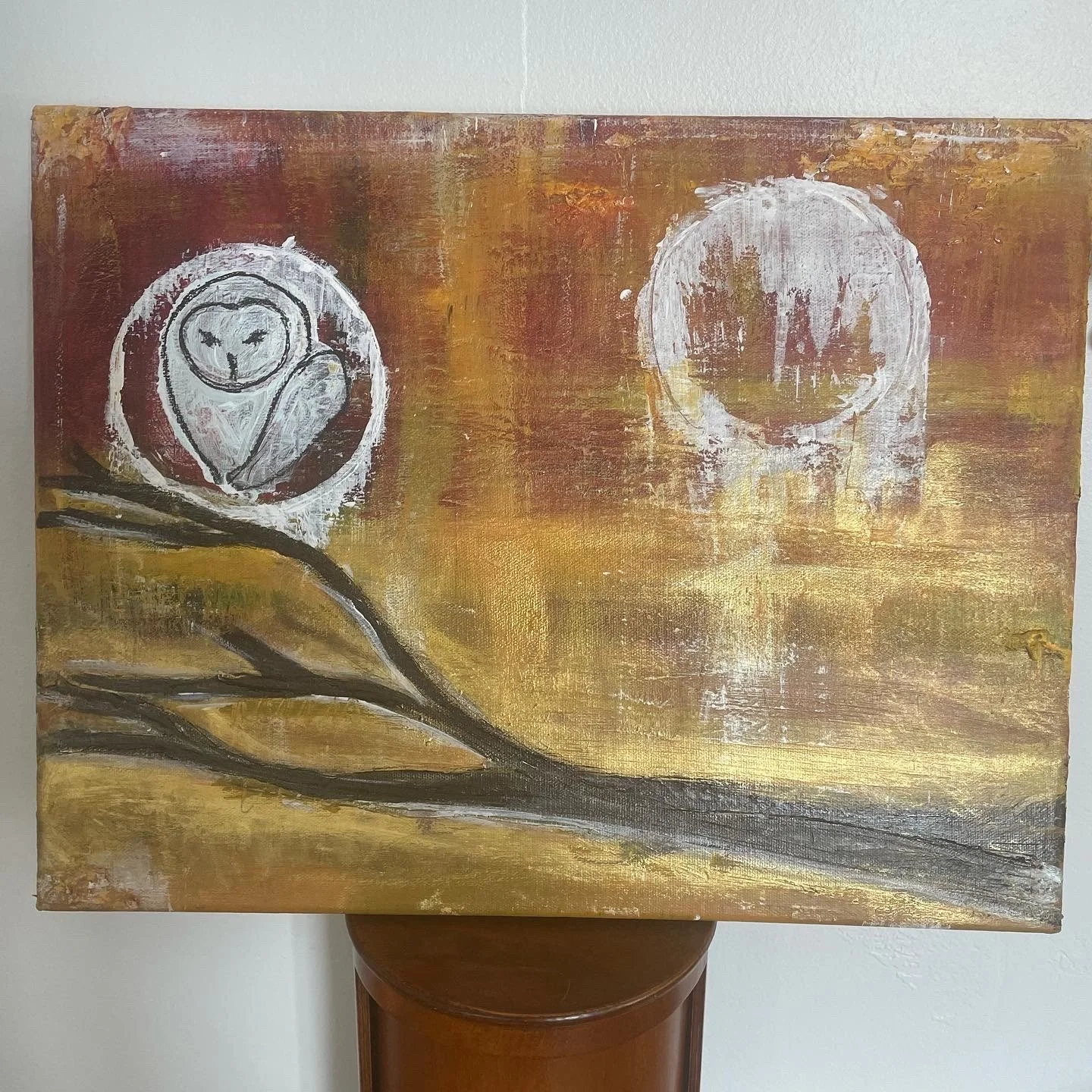 Abstract painting with two white circle shapes on a textured brown, orange, and gold background, featuring a brown branch with a white flower in the lower left corner.