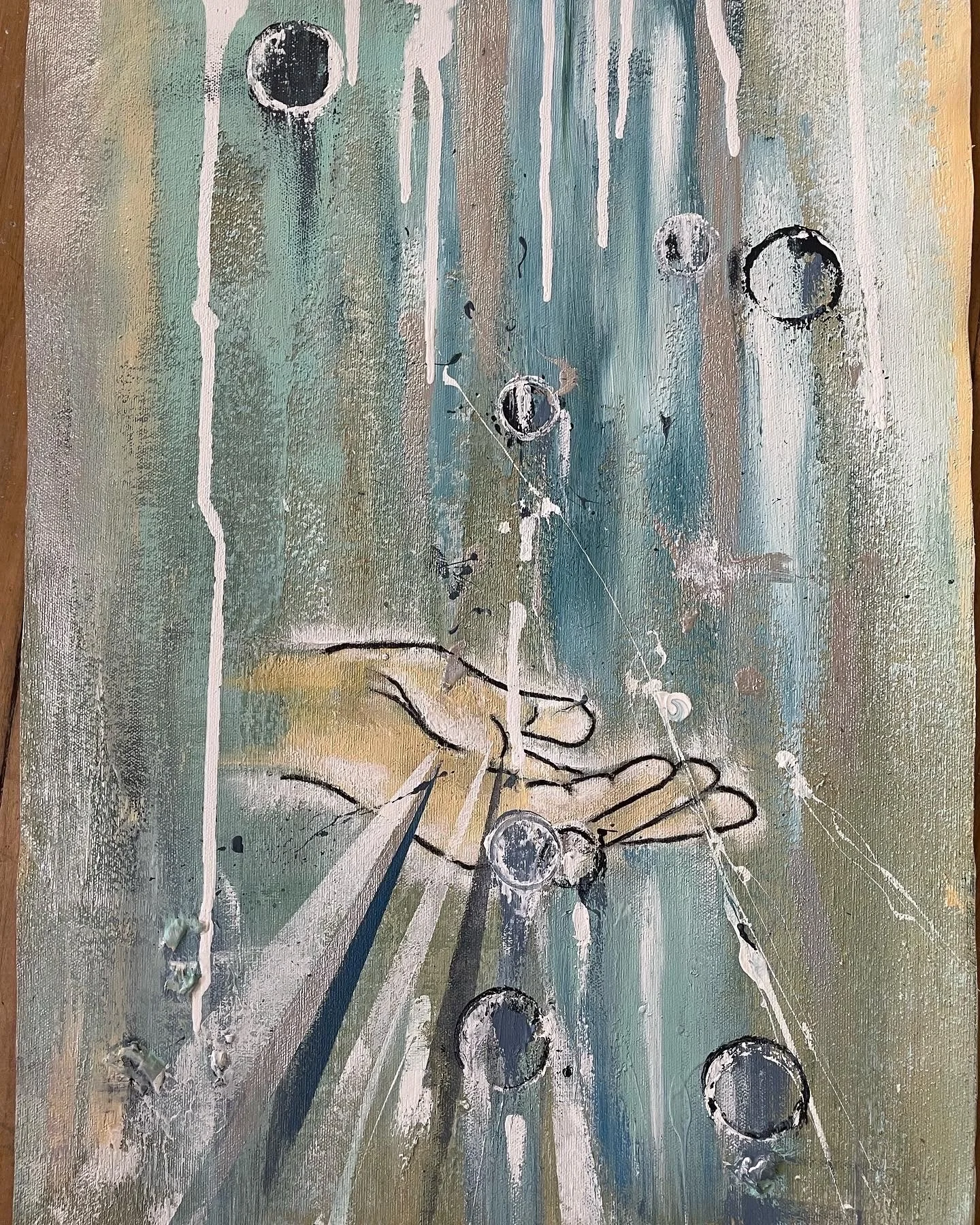 An abstract painting with a background of blended muted colors including green, blue, beige, and white. There are several black and white circles, some containing horizontal lines, scattered across the canvas. White drips and splatters are also prese