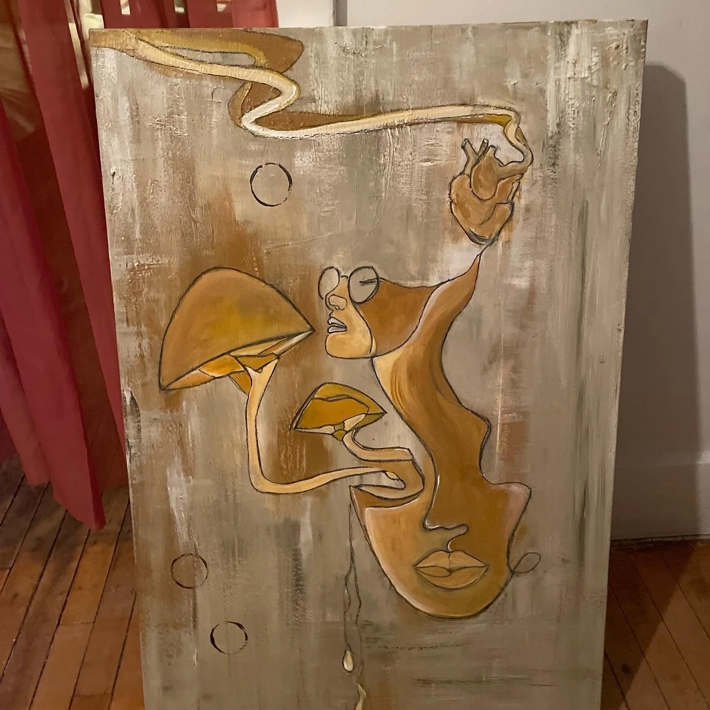 Abstract artwork featuring a line drawing of a woman's face with glasses, flowing hair, and lips, incorporating leaves and circles in shades of brown, beige, and gold on a distressed, painted wooden background.