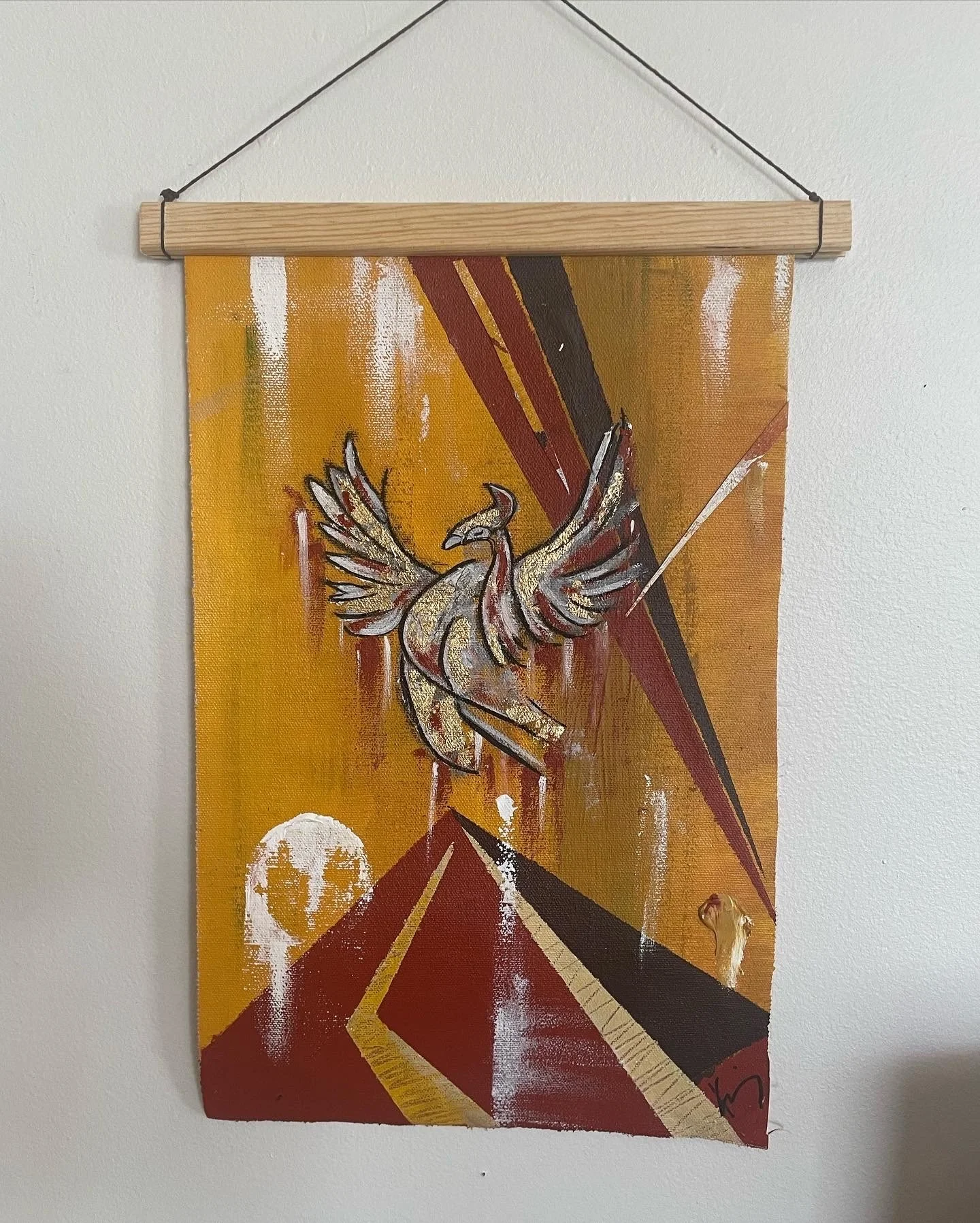 Abstract painting featuring a stylized bird with wings spread, set against a background of red and orange streaks, with white circles and a peace symbol, hung on a white wall.
