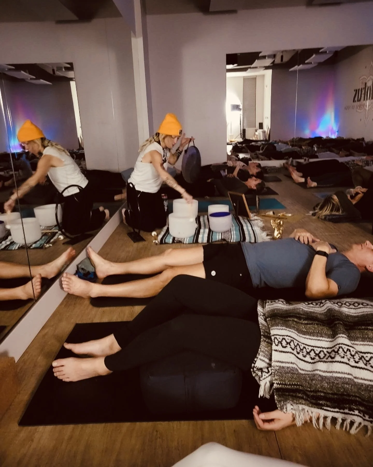 Sound Bath in Omaha NE. People lying on yoga mats during a yoga class, with a woman in a yellow beanie playing singing bowls.