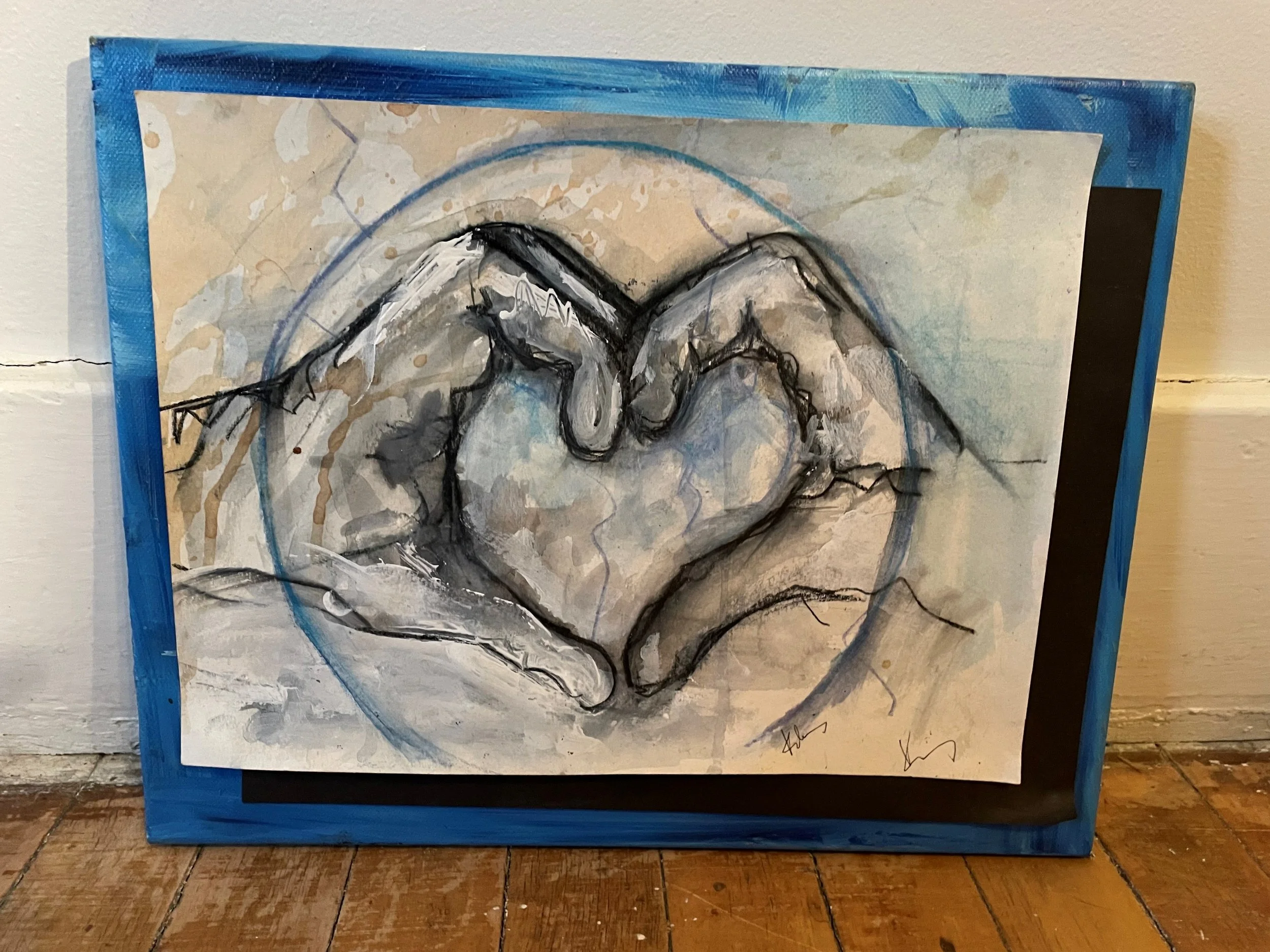 Abstract painting of a face with black outlines, blue, beige, and gray tones, framed with blue trim, leaning against a wall on a wooden floor.