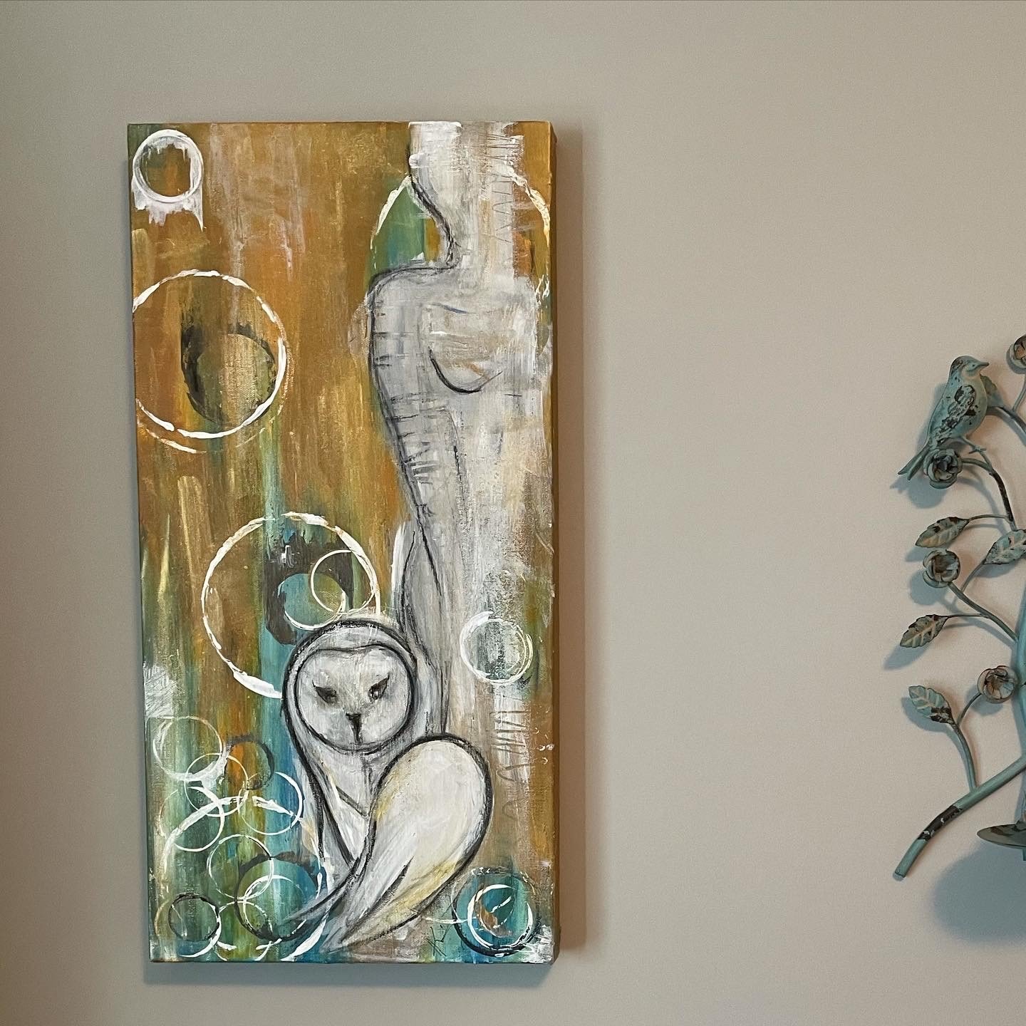 Abstract painting of a white cat with black eyes and nose, surrounded by circles and colorful backgrounds on a vertical canvas, displayed on a beige wall.