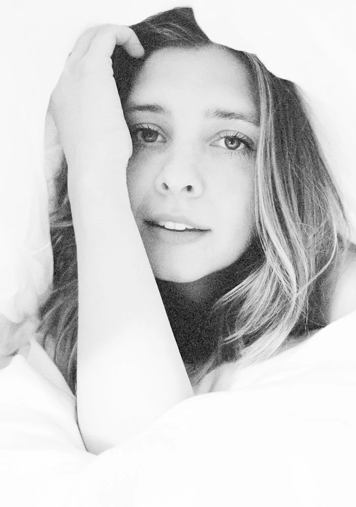 Black and white portrait of a young woman with long hair, resting her head on her hand, looking at the camera with a soft expression.