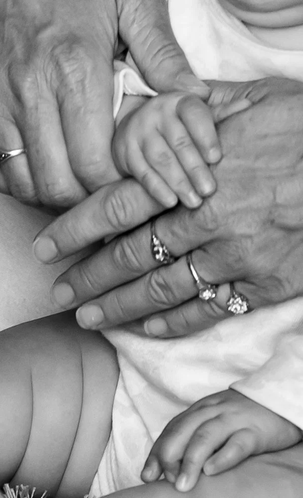 Close-up of a child's hand holding an older person's hand, both wearing rings, in black and white.