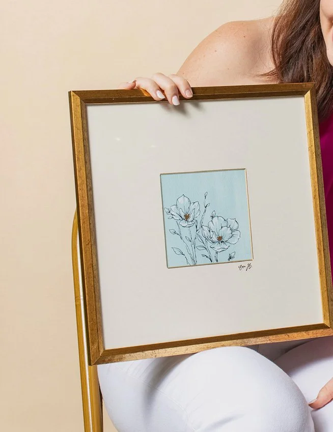 framed floral artwork of magnolias on a blue background with gold accents.