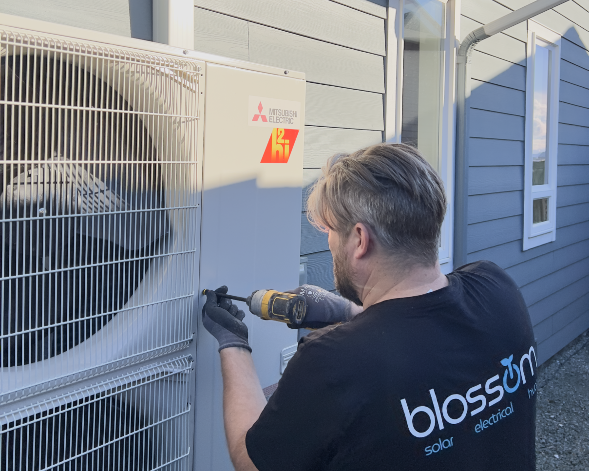 Blossom solar installer wearing a blossom solar electrical hvac shirt installing a Mitsubishi heat pump outside at dusk.
