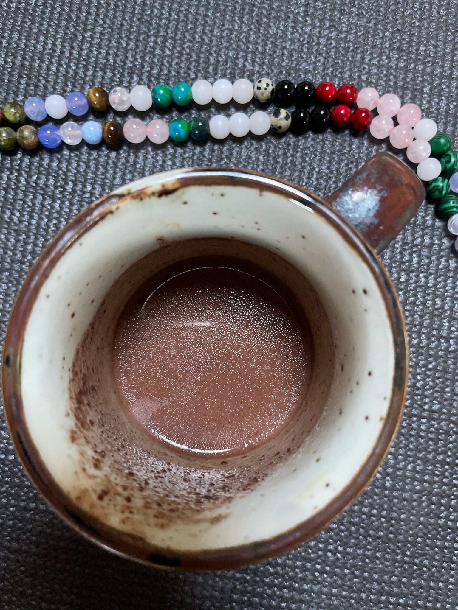 Empty coffee mug with remnants of beverage inside, placed on a textured surface, with a colorful beaded necklace laying nearby.