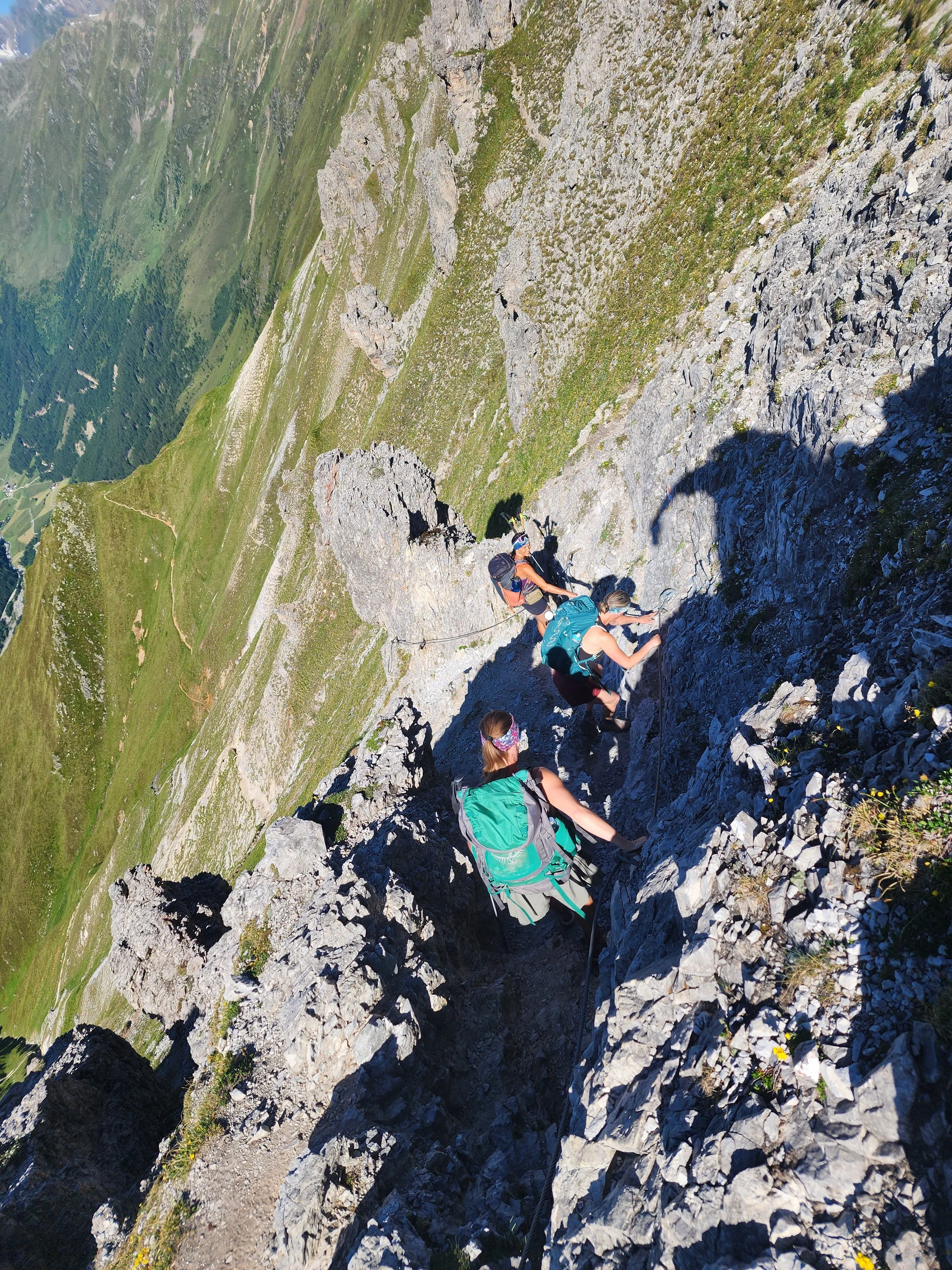 Four hikers equipped with backpacks and climbing gear ascending a steep rocky mountain trail.
