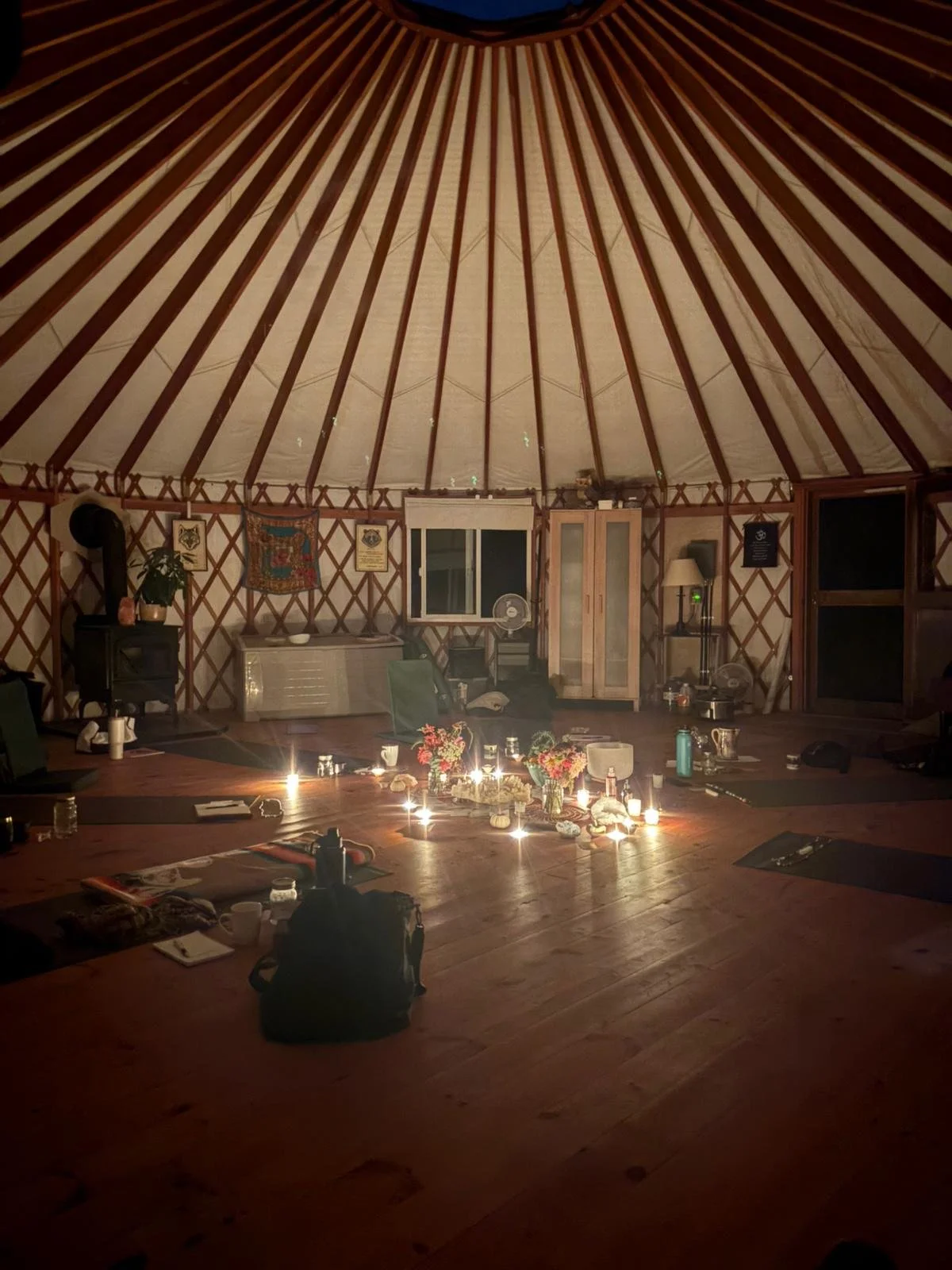 Interior of a yurt with candles, flowers, and personal items arranged on the floor for a gathering or ceremony.