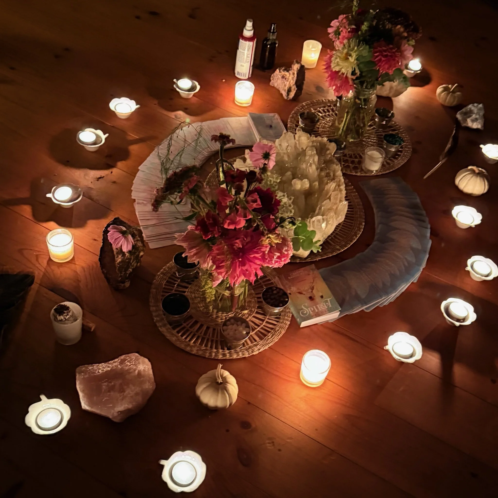 A cozy table setup on a wooden floor with candles, flowers, pumpkins, and stones, creating a warm, inviting atmosphere.