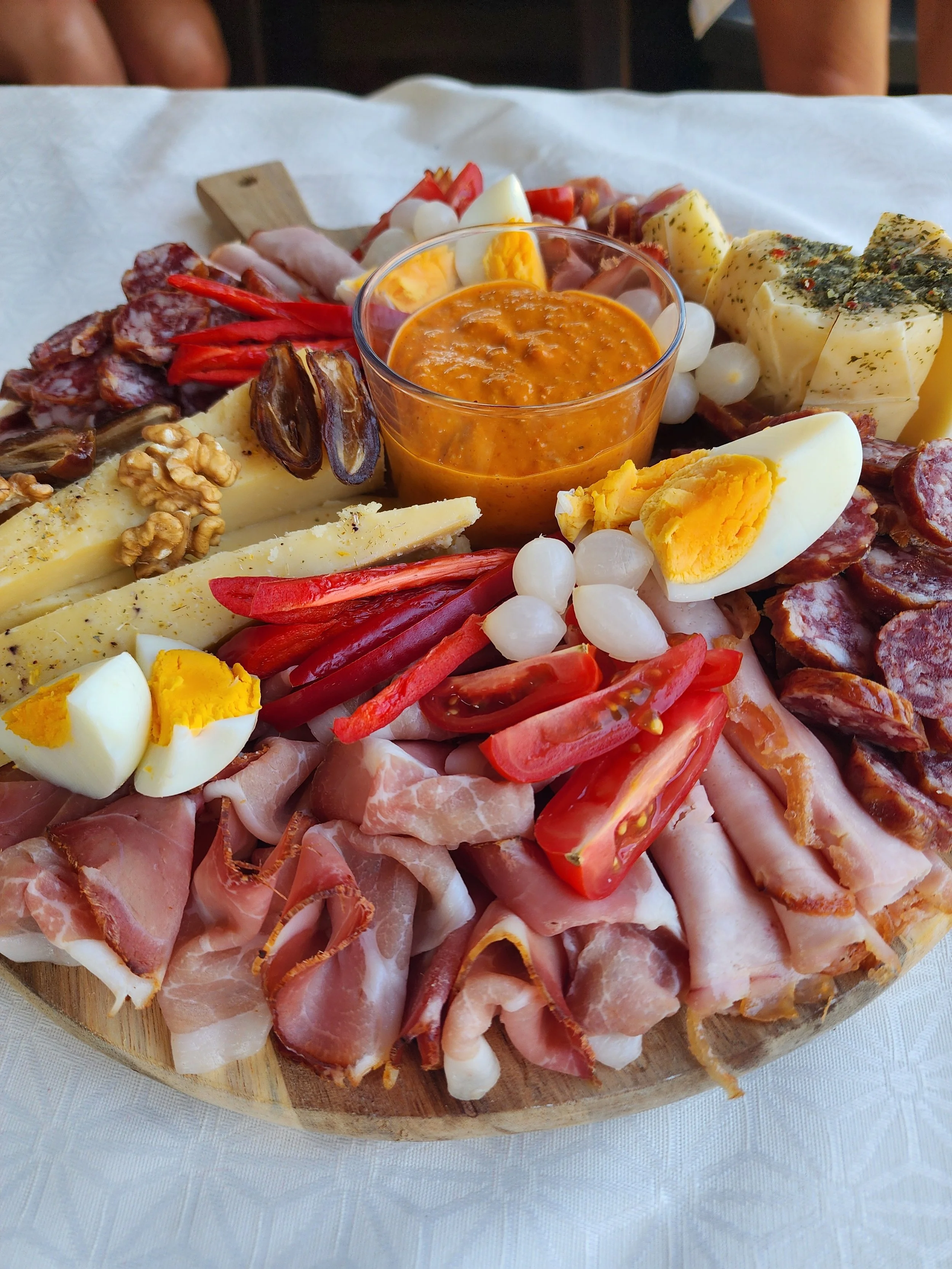 Charcuterie board with cheeses, meats, boiled eggs, cherry tomatoes, red peppers, walnuts, dried figs, and a small bowl of orange sauce