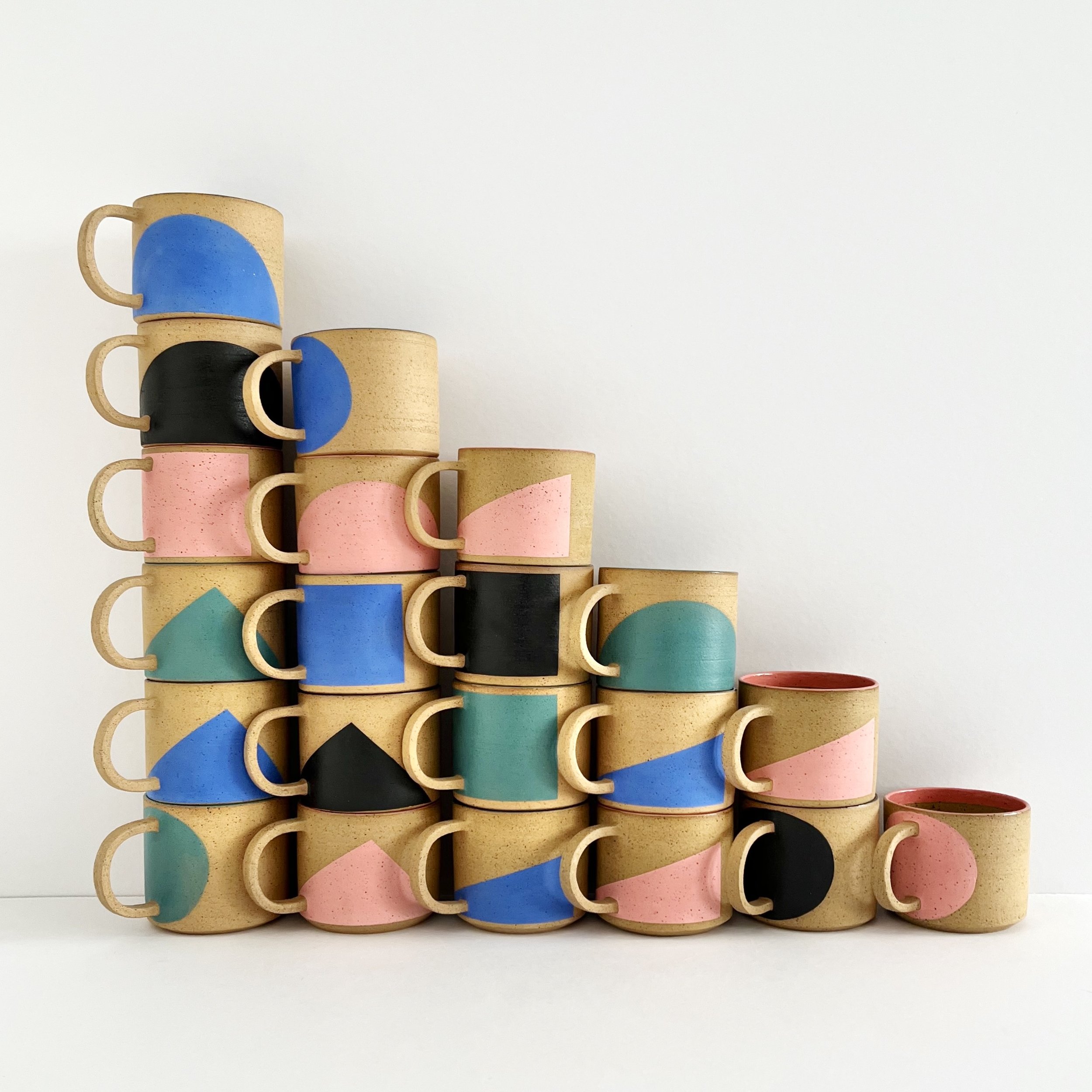 Varias tazas de cerámica con diseños abstractos y colores pastel apiladas en forma de pirámide sobre fondo blanco. Club de tazas LODAZAL- colección de temporada