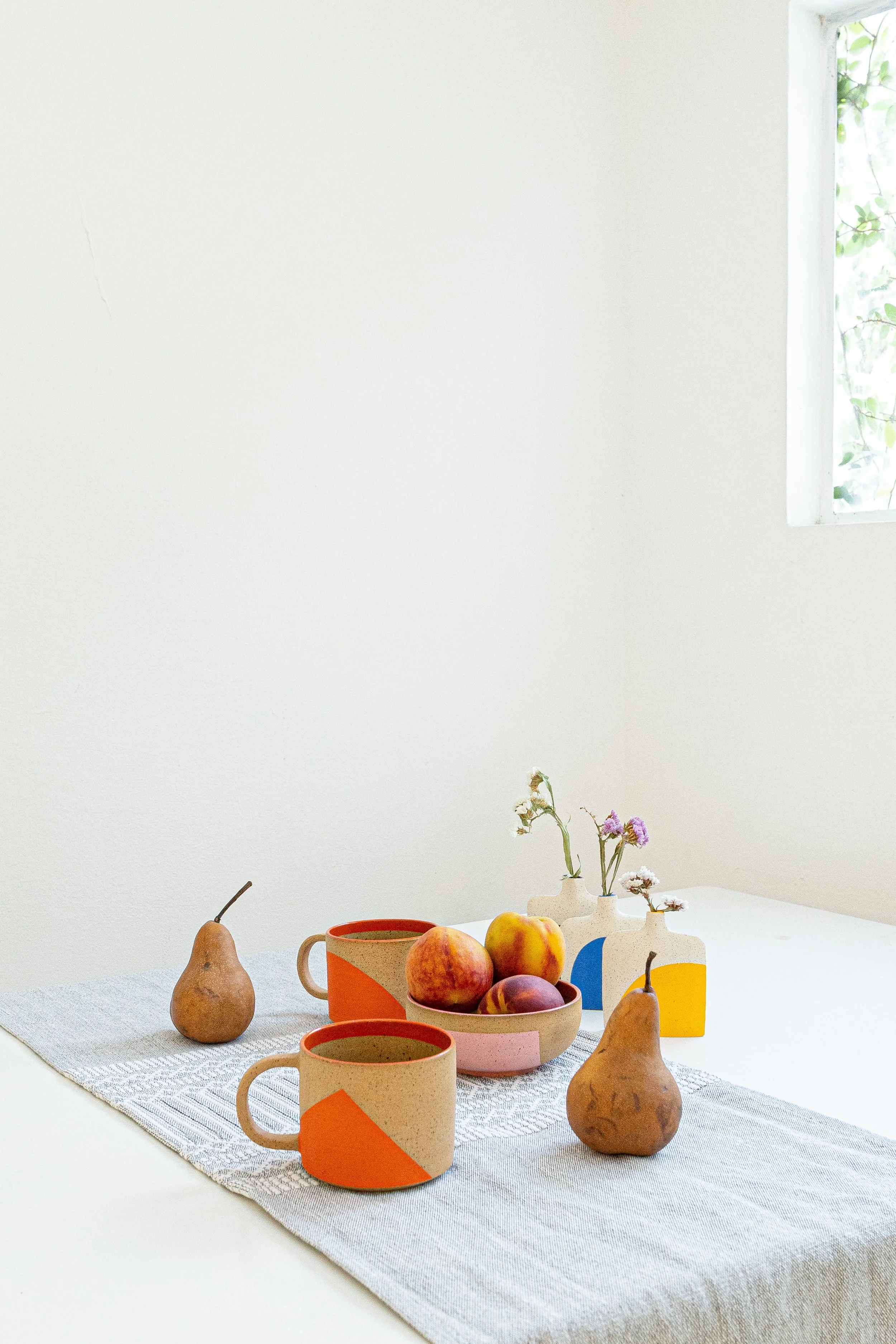 Mesa con cerámica de colores y peras, en un ambiente con luz natural y ventana.