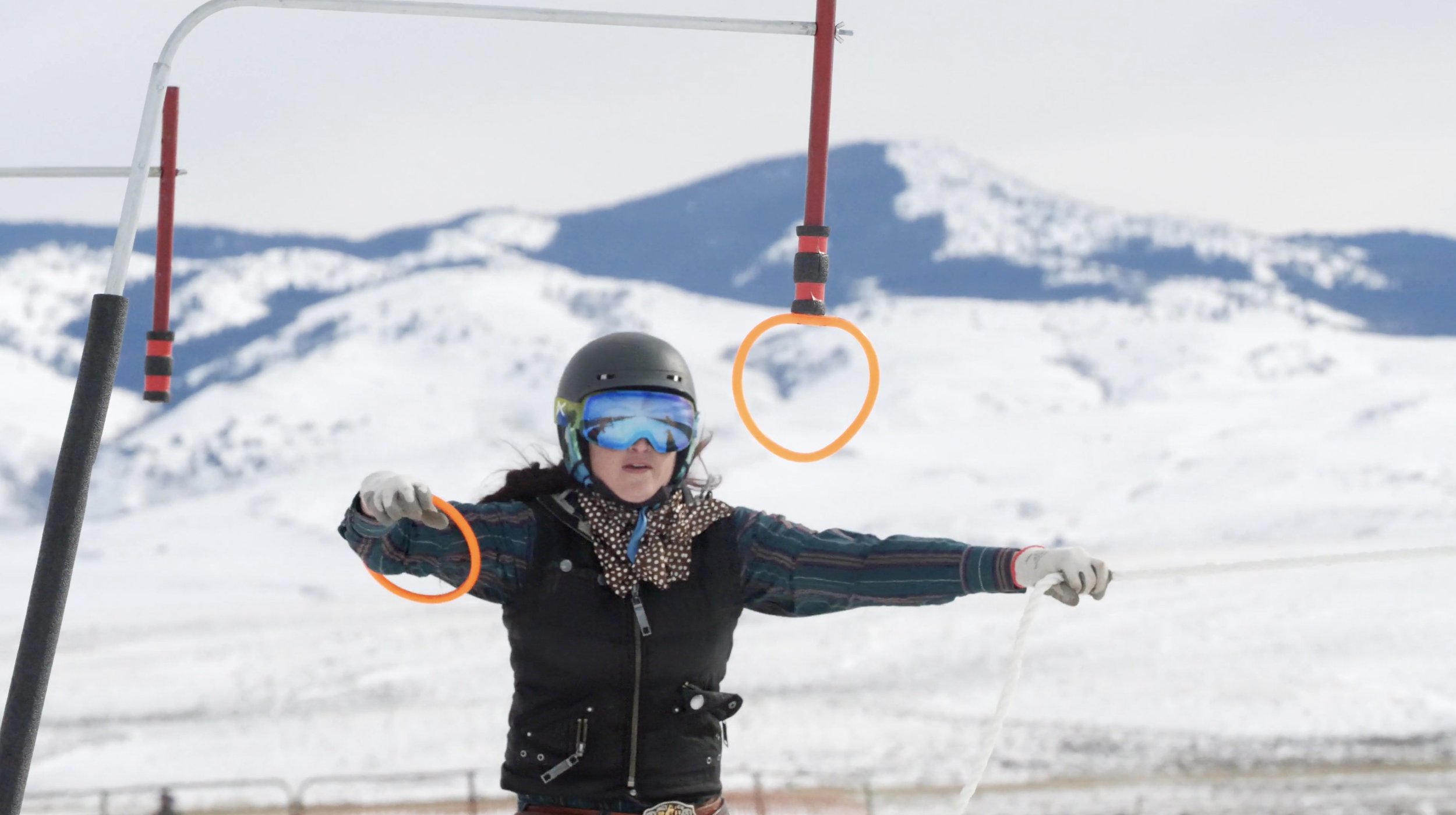 Person wearing ski gear catching a ring with a rope in a snowy landscape.
