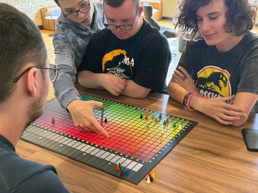Brilliant Breakfast Club participants play a colorful board game together, discussing moves and collaborating around a table in the studio.