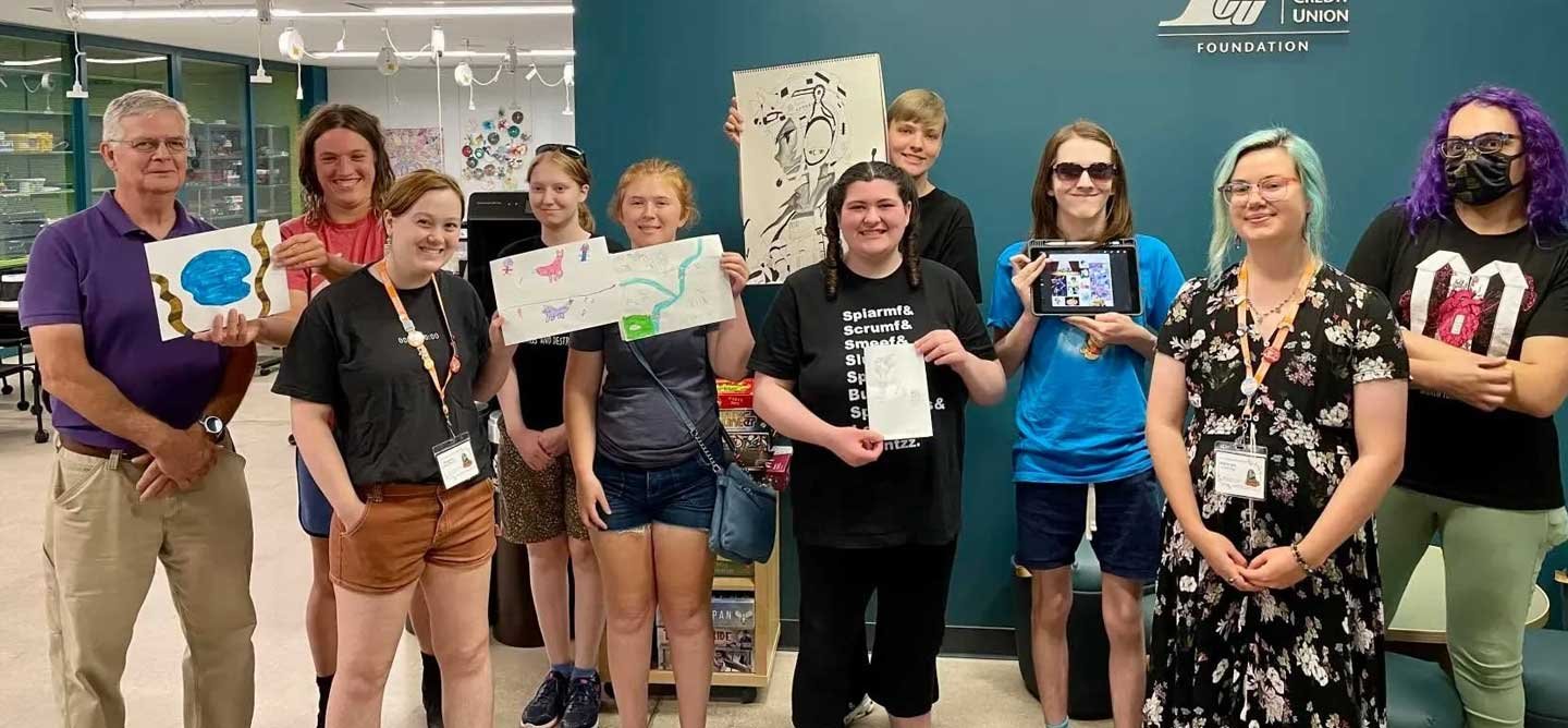 IOB participants, mentors, and community partners pose together holding artwork during a Fellowship Program celebration in Eau Claire, Wisconsin.