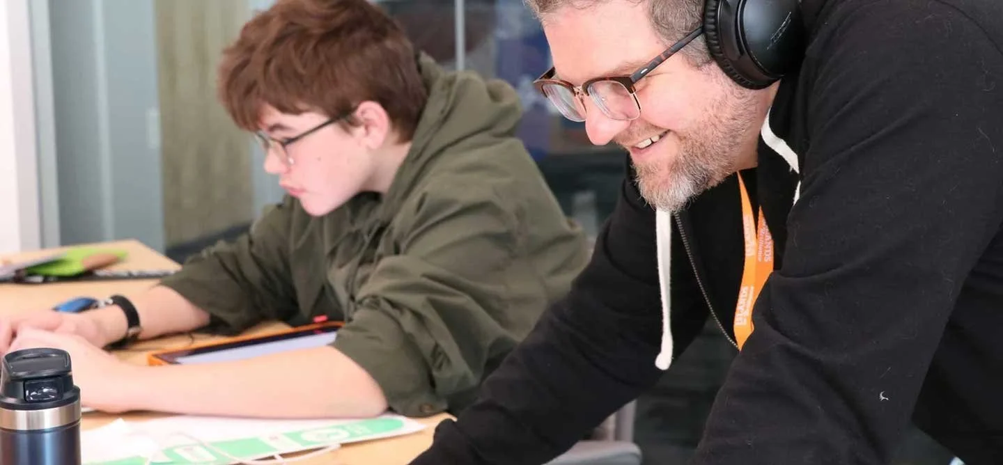 An IOB mentor supports a student working on a digital design project during SideQuest, focused on building creative software skills in the studio.