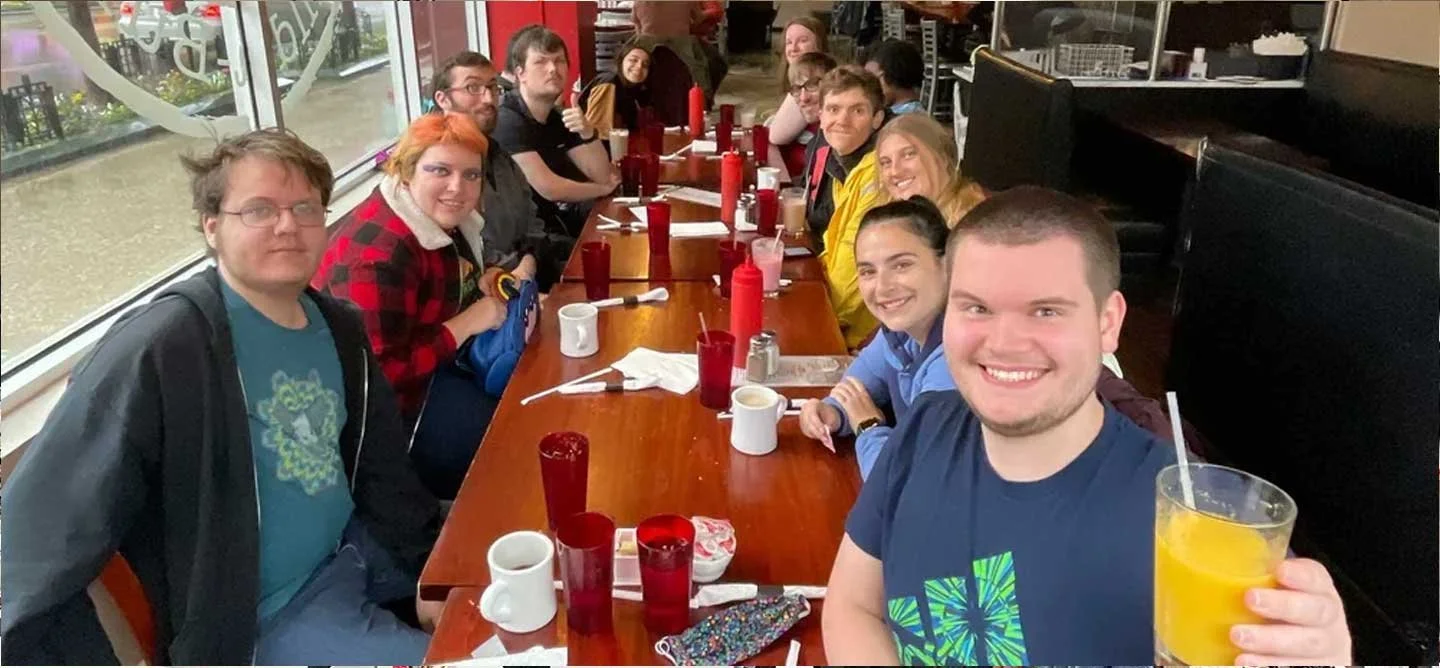 Brilliant Breakfast Club participants gather for breakfast at a restaurant, smiling together and building community during an in-person meetup.