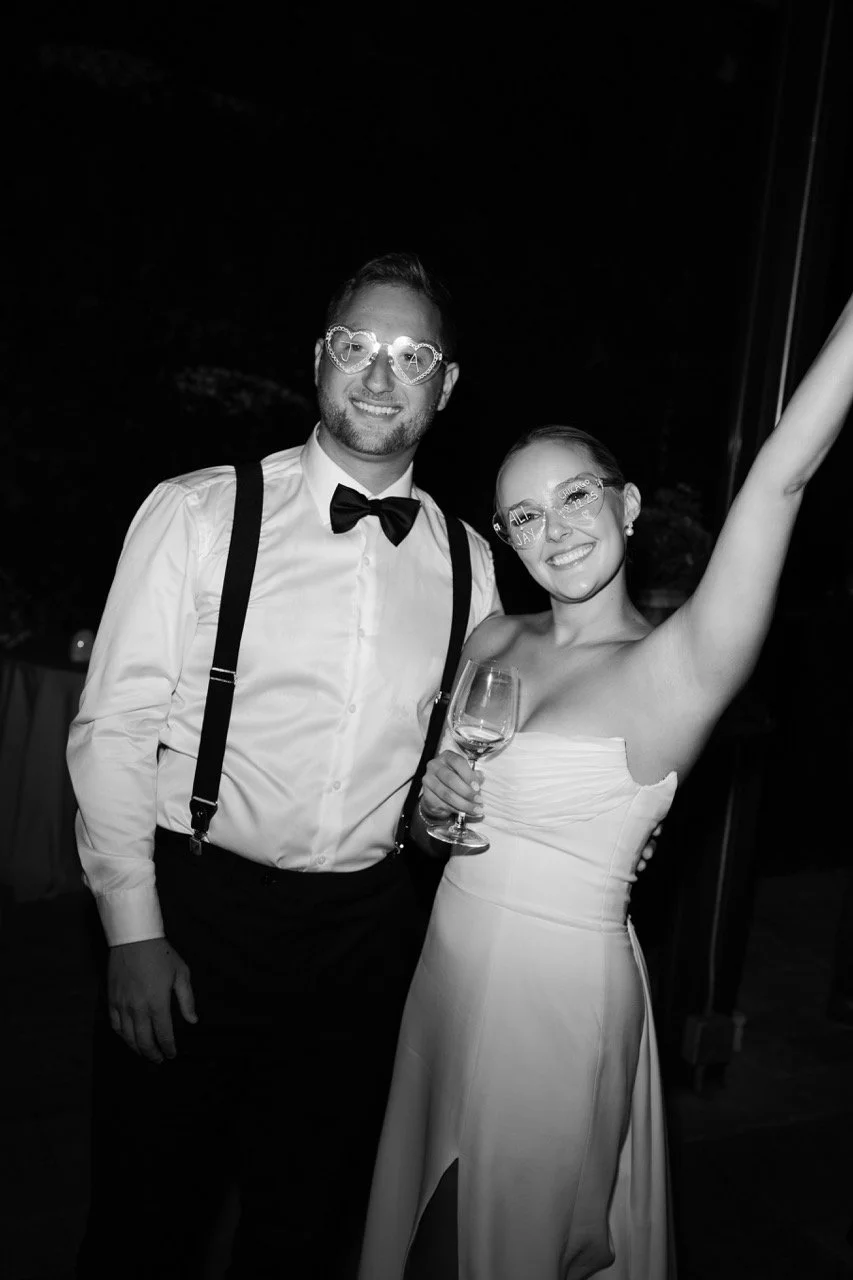 black and white photo of couple smiling and bride's hand up with personalized sunglasses for wedding reception dancing