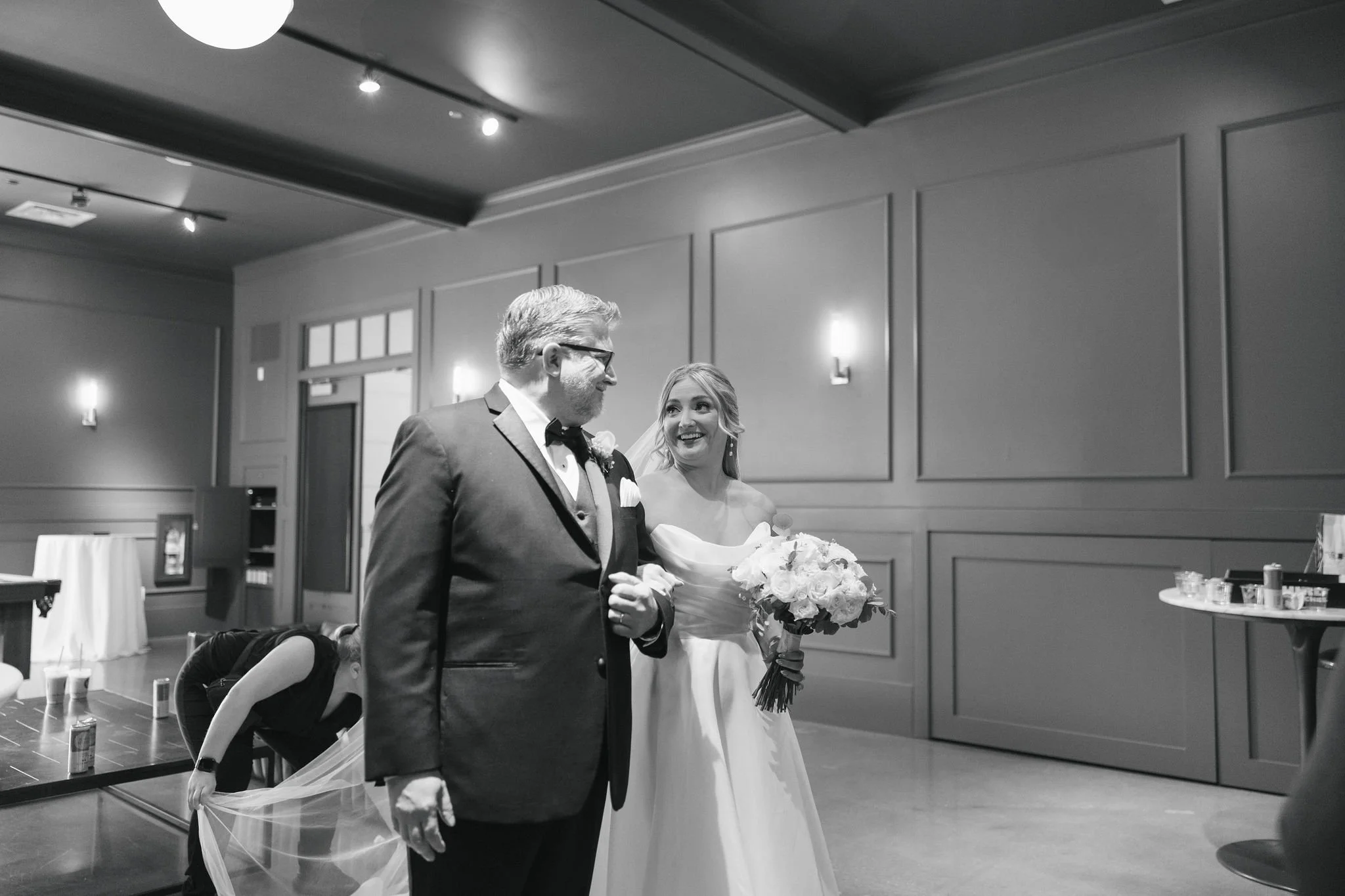 Black and white photo bride and father of bride looking at each other before processional while wedding coordinator places veil on ground