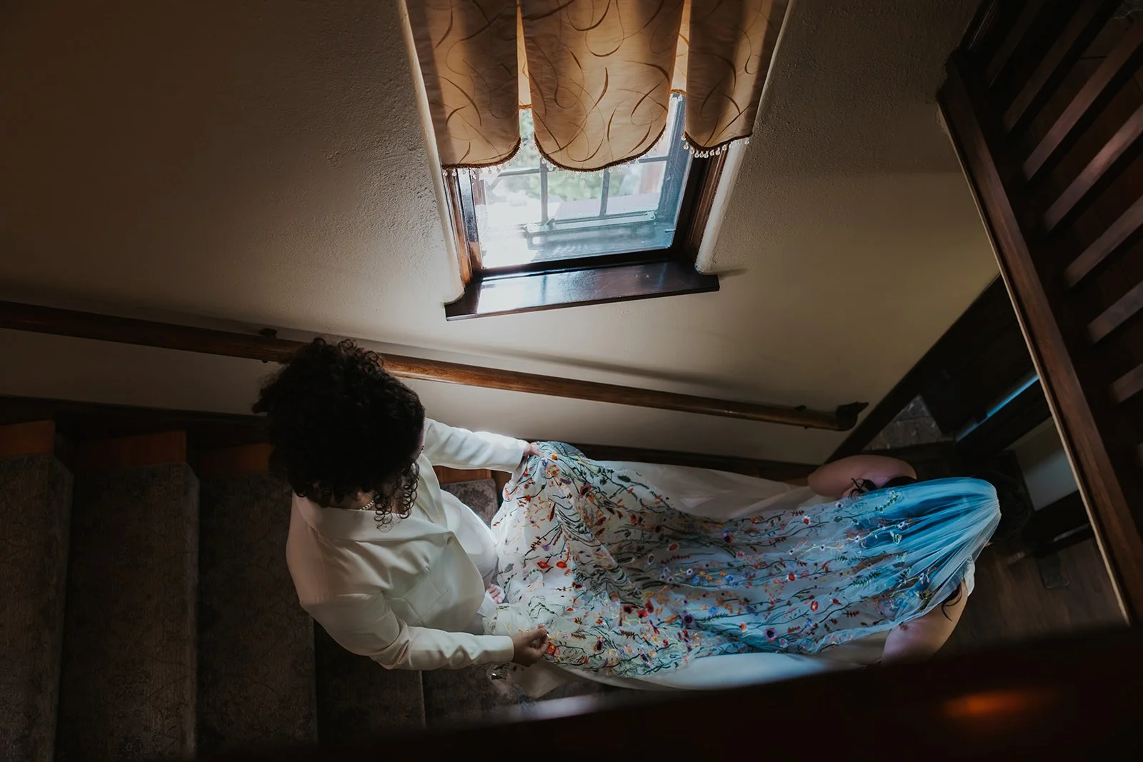 two brides going down stairs and bride in suit is holding bride in dress veil