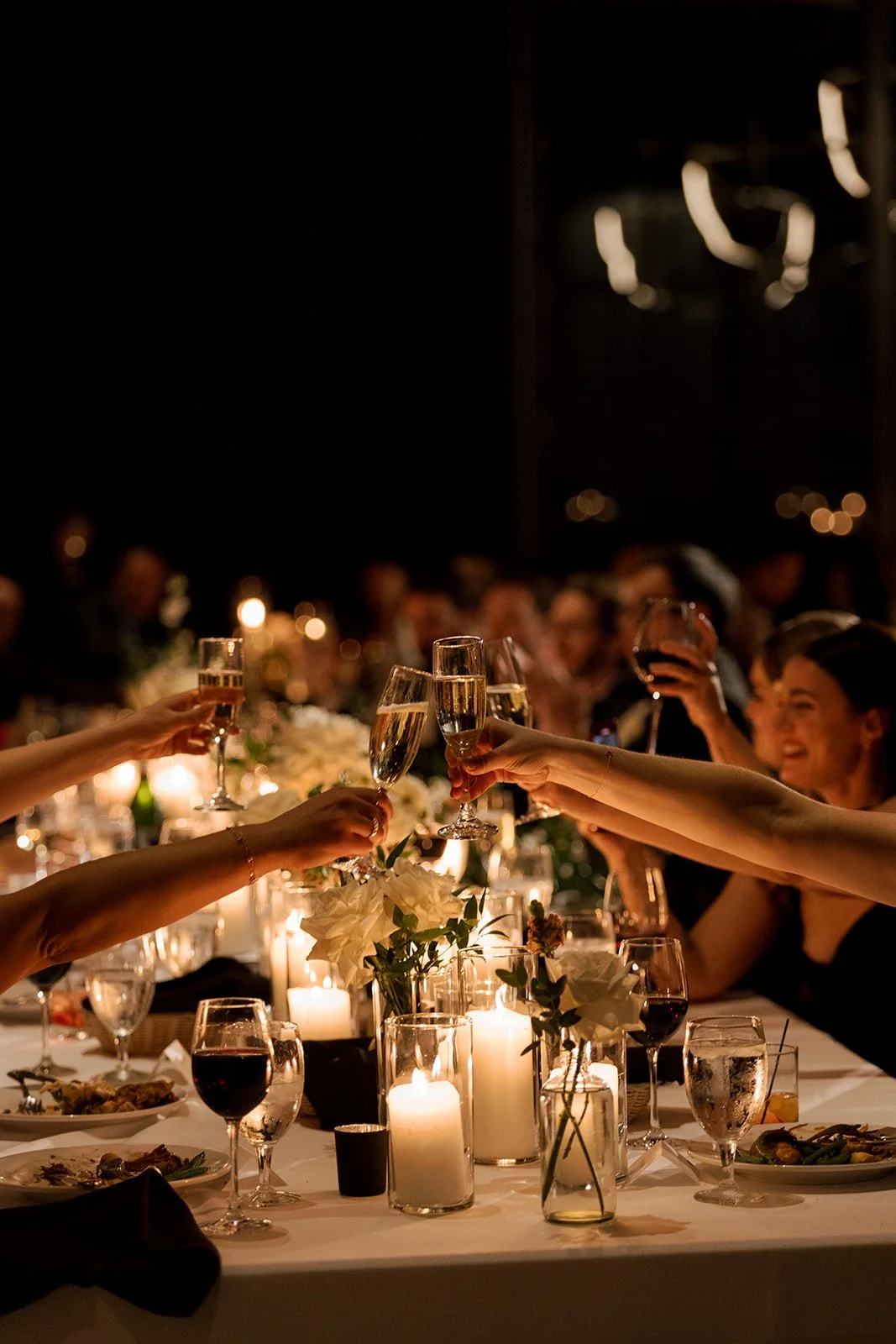 Wedding guests toasting and cheersing with drinks at romantic candlelit dinner