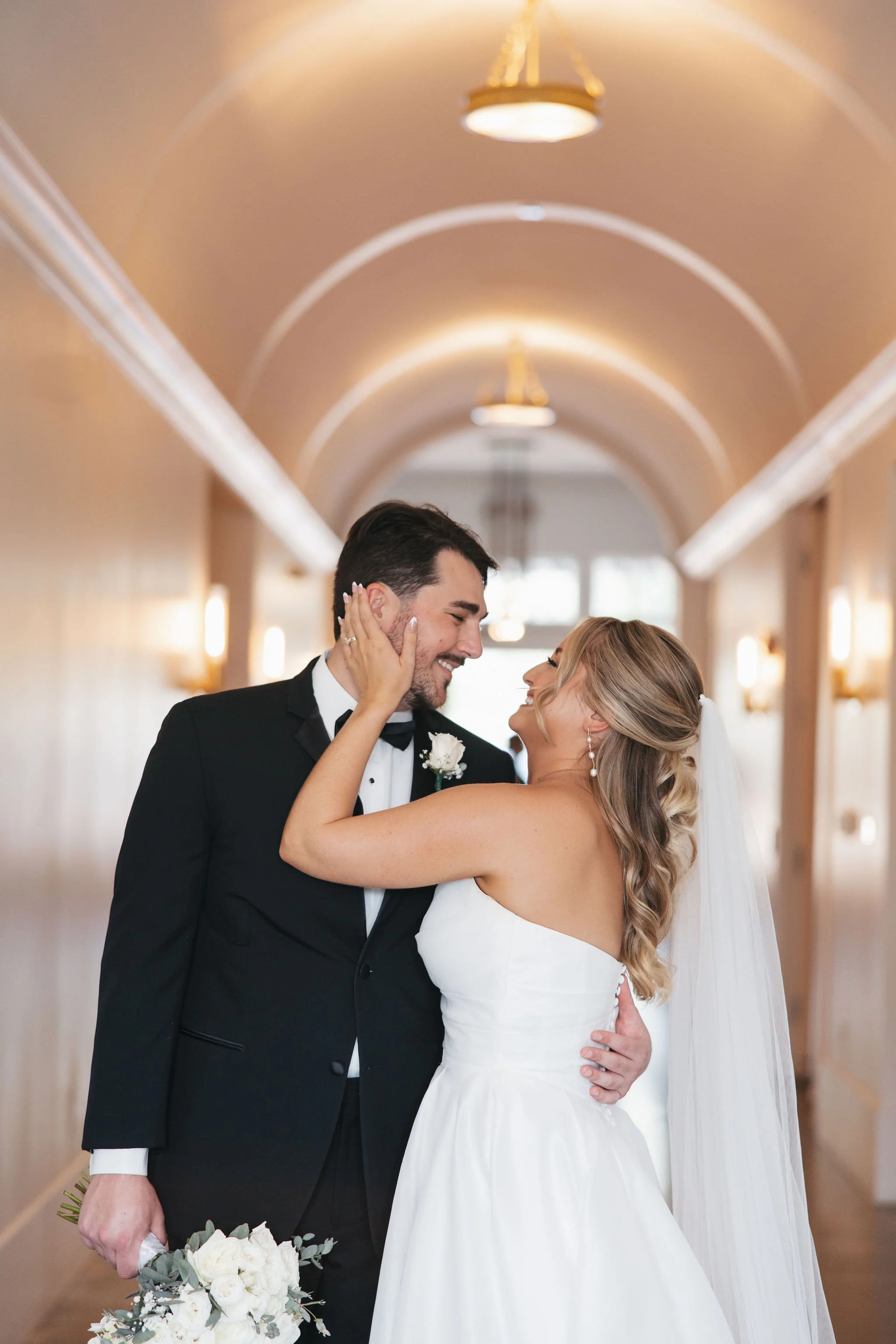 Bride holding the groom's face and smiling at each other in hallway