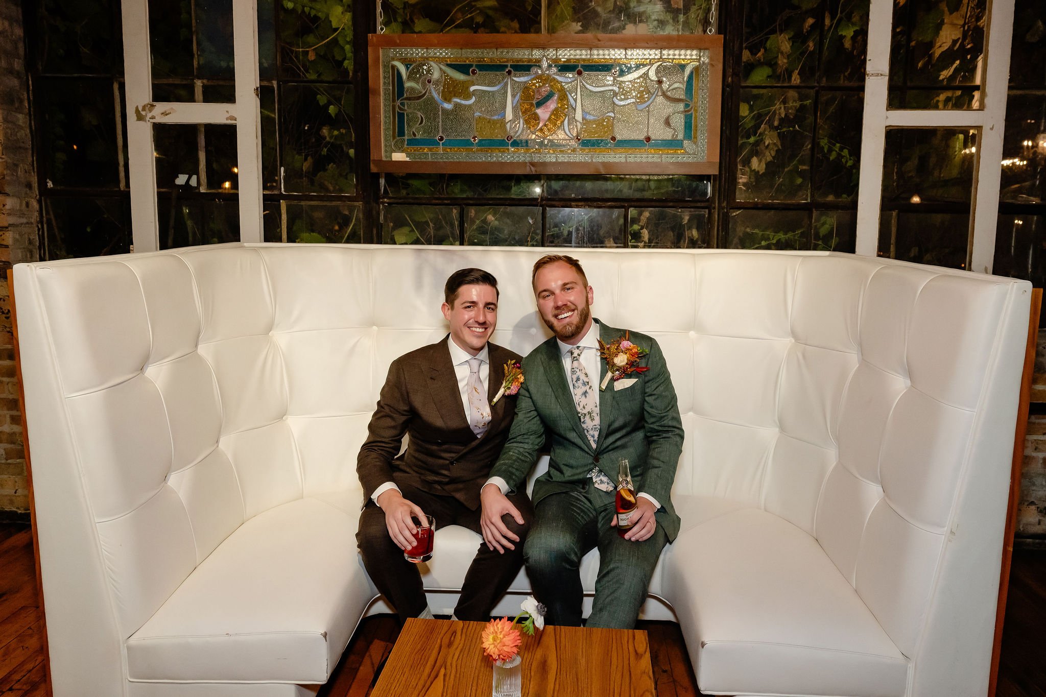 unique vintage white booth couch with two grooms sitting and smiling at camera
