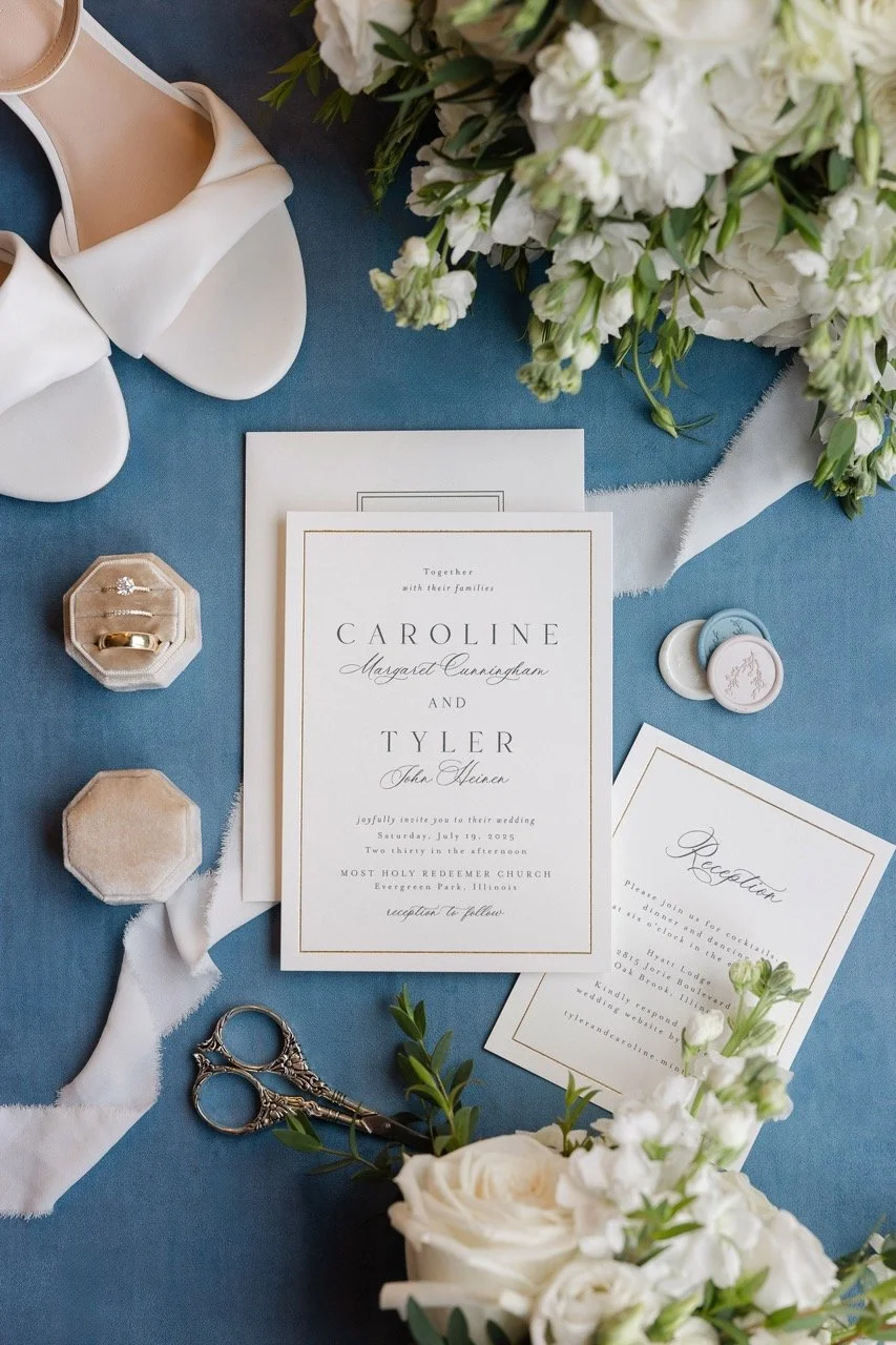 Blue background with white wedding invitation, shoes, flowers, and rings