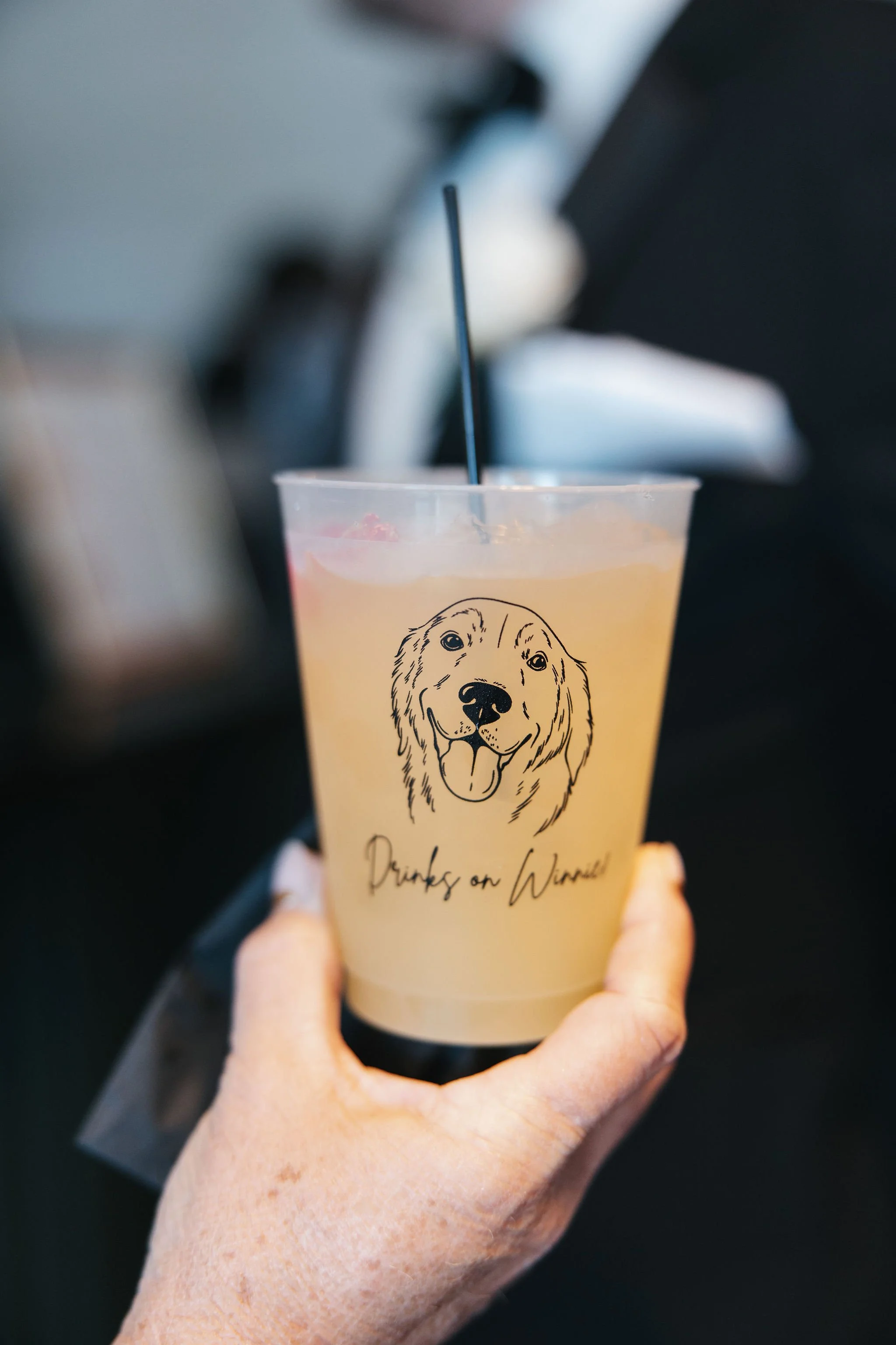 Clear plastic cup with golden retriever dog printed on it and says "drinks on Winnie"