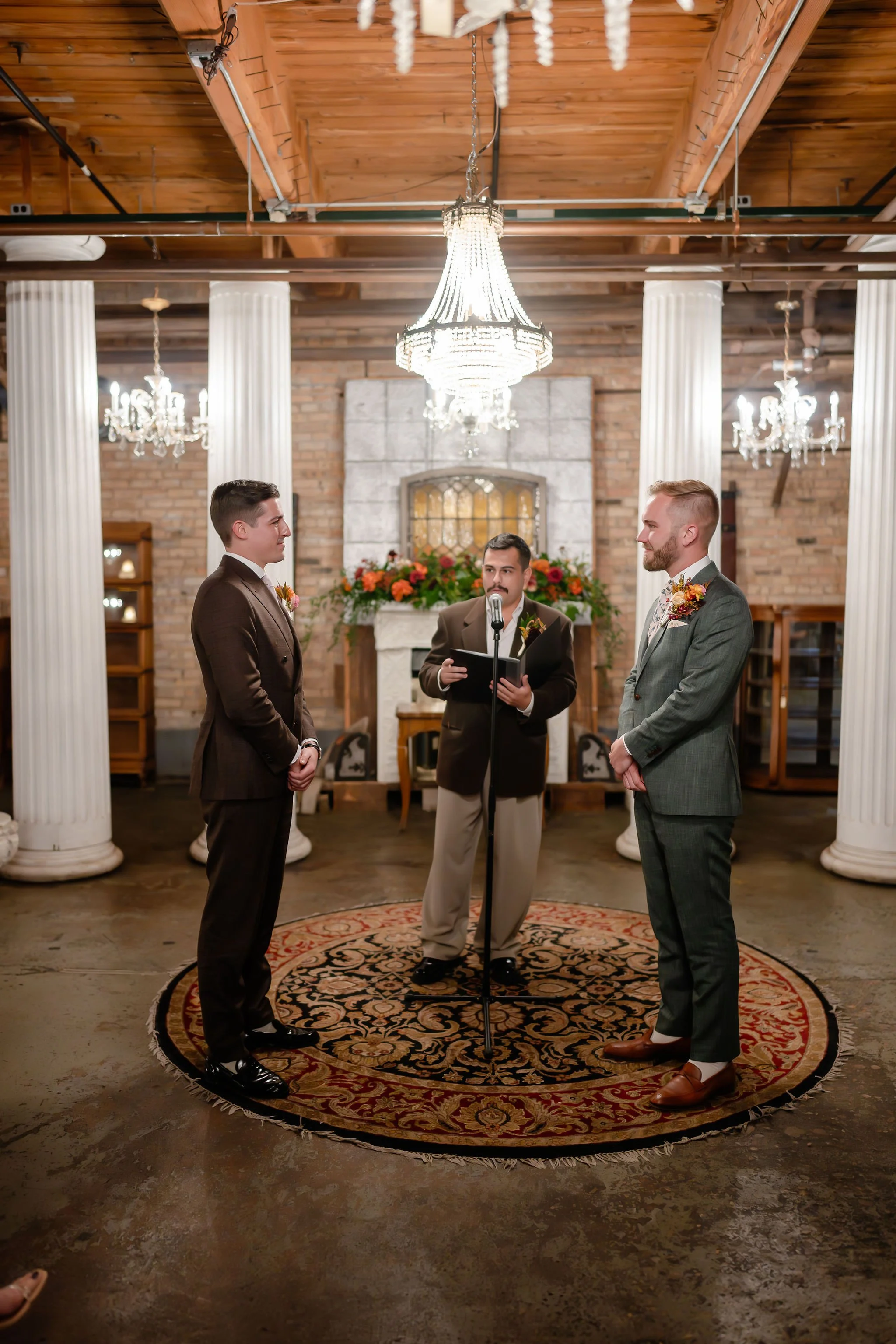 Wedding ceremony with officiant and two grooms standing facing each other on vintage rug