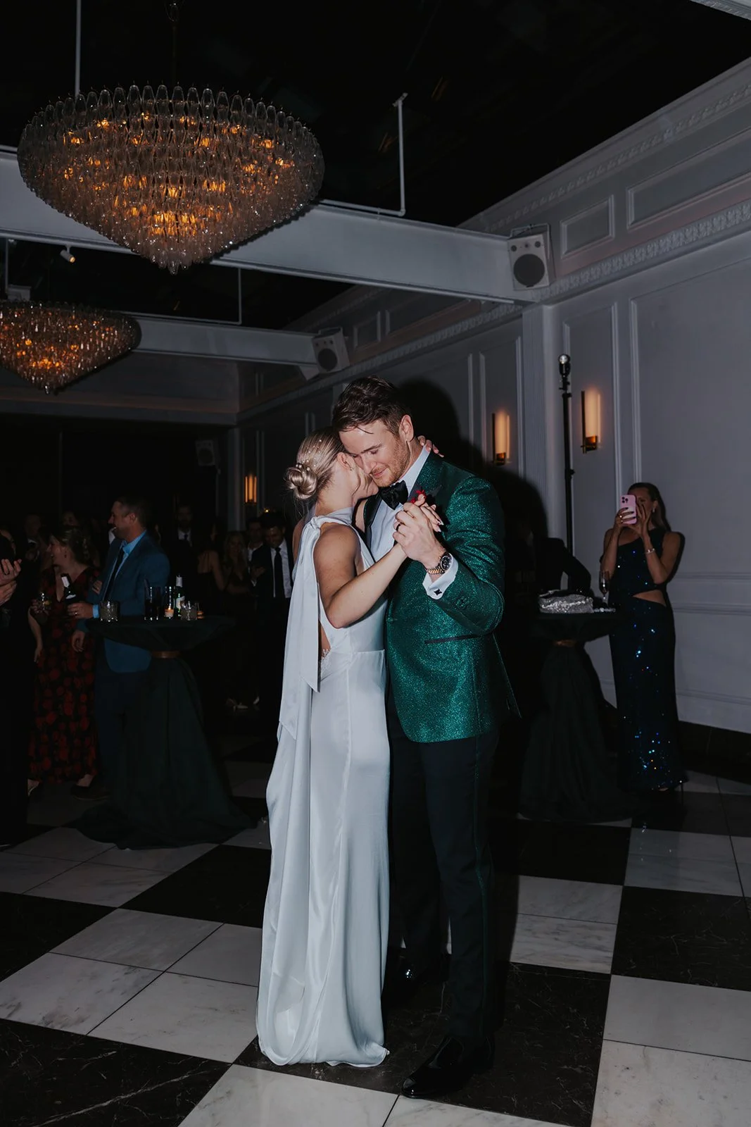 couple's first dance on black and white checkered dance floor with guests in the background