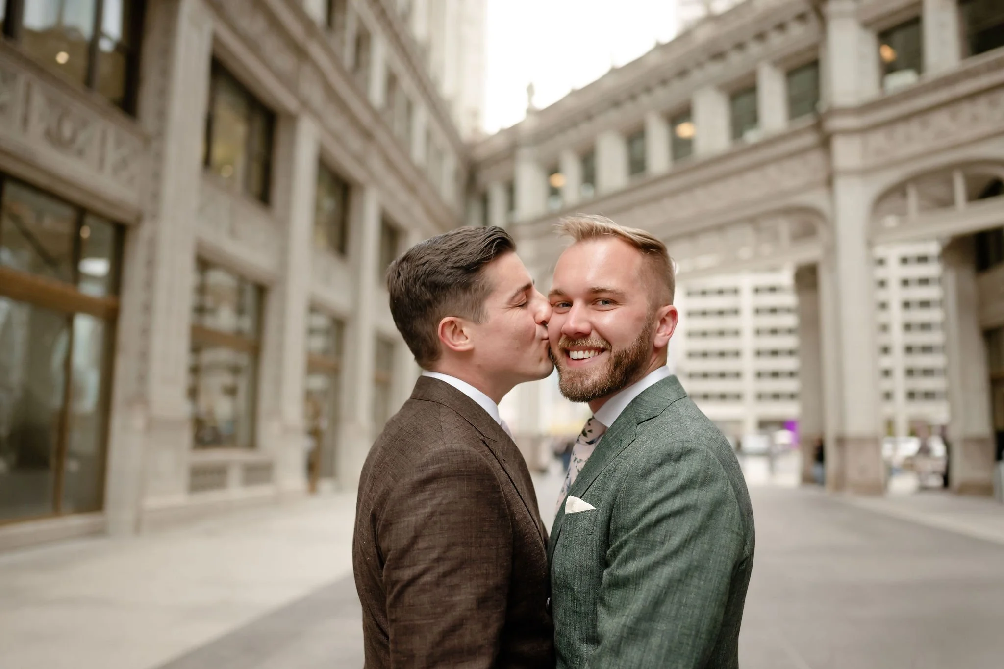 Groom kissing groom's cheek while smiling together for couple's portraits