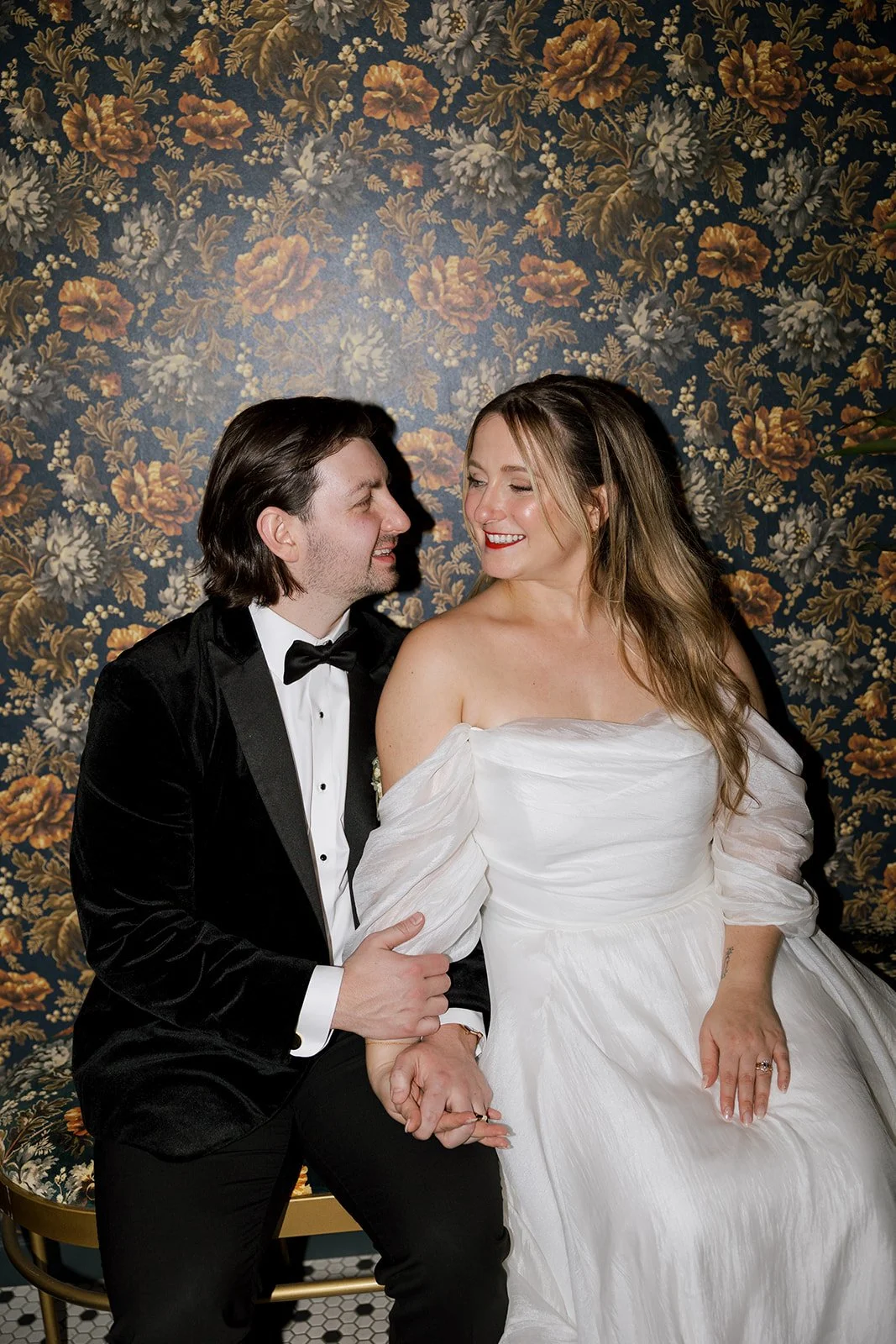 Bride and groom holding hands smiling with floral print wall as background at Wildman BT in Chicago