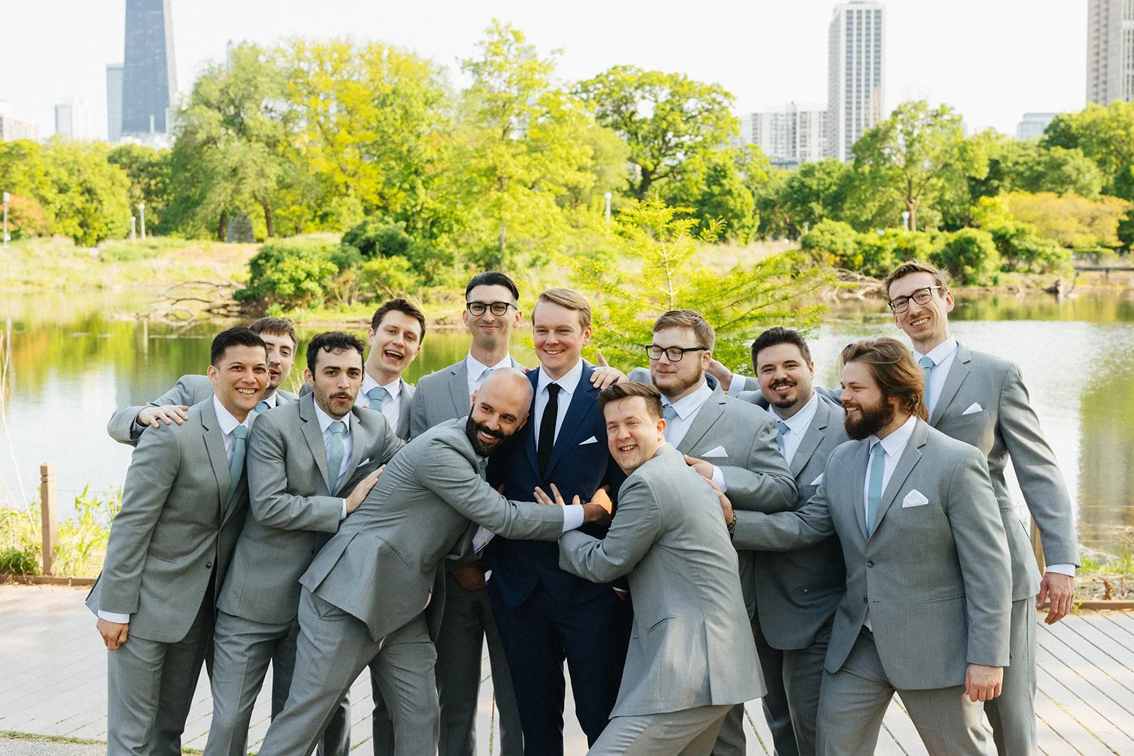 Groomsmen crowding around groom smiling outdoors in Lincoln Park Zoo in Chicago
