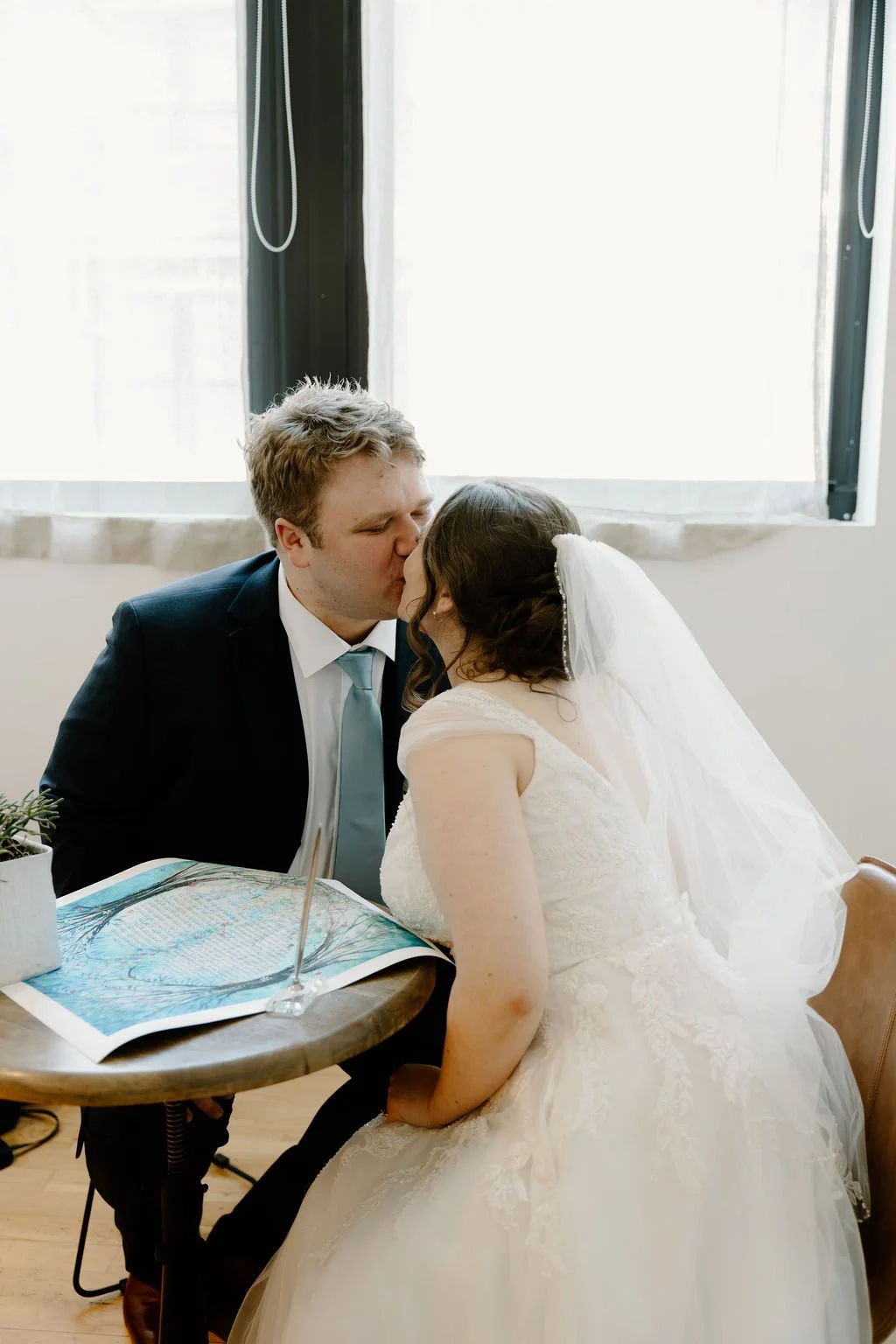 Jewish wedding tradition of signing the ketubah, bride and groom seated next to it and kissing