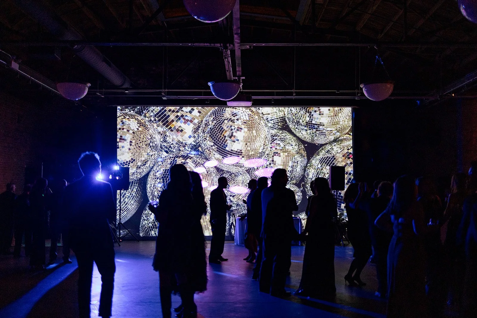 Disco ball photo on dance floor projector wall with wedding guests standing in front