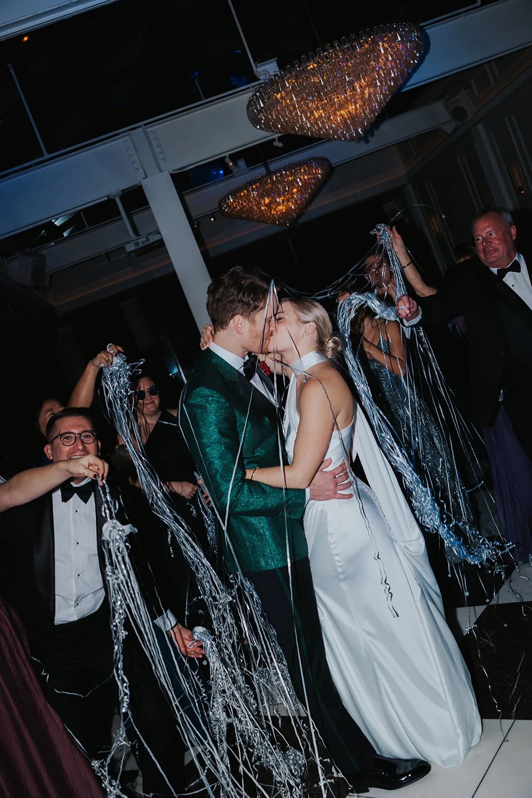 bride and groom kiss with streamers thrown on and around them