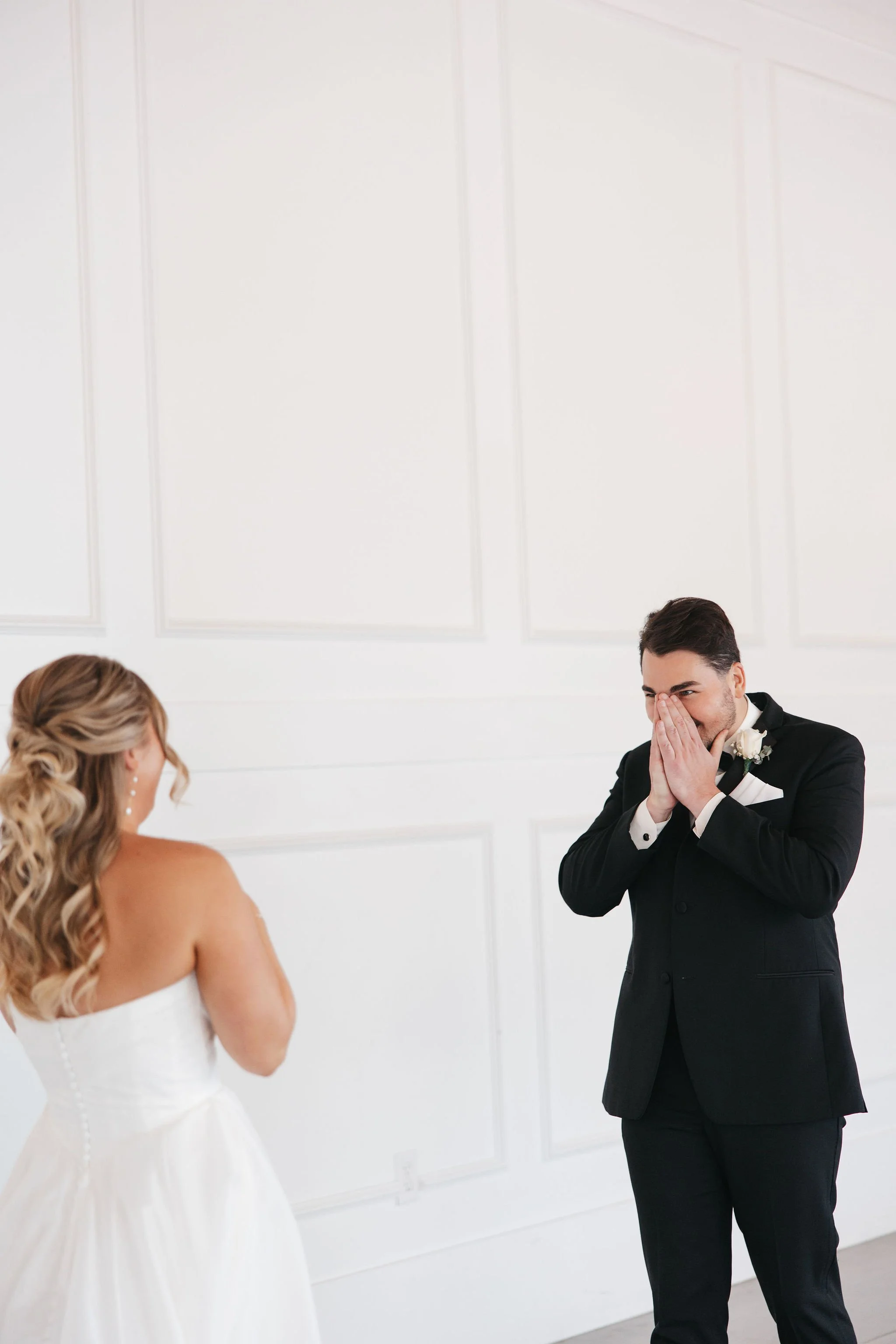 Groom smiling and holding hands in front of face taking in bride at first look