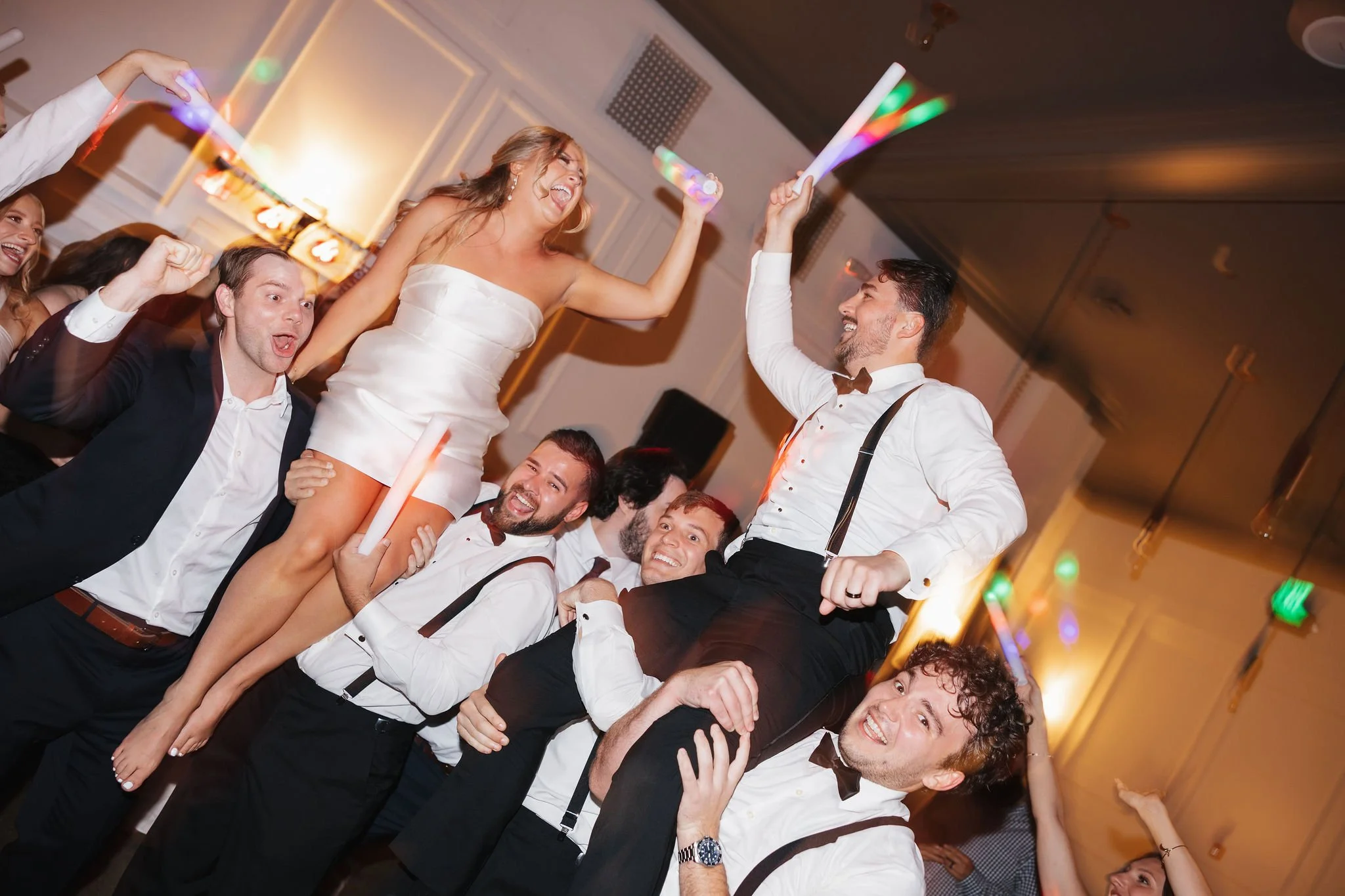 Bride and groom on wedding guests' shoulders with everyone cheering and waving glow sticks