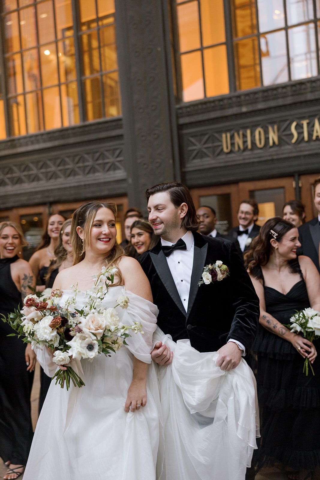 Couple smiling outside Union Station in Chicago with wedding party behind them