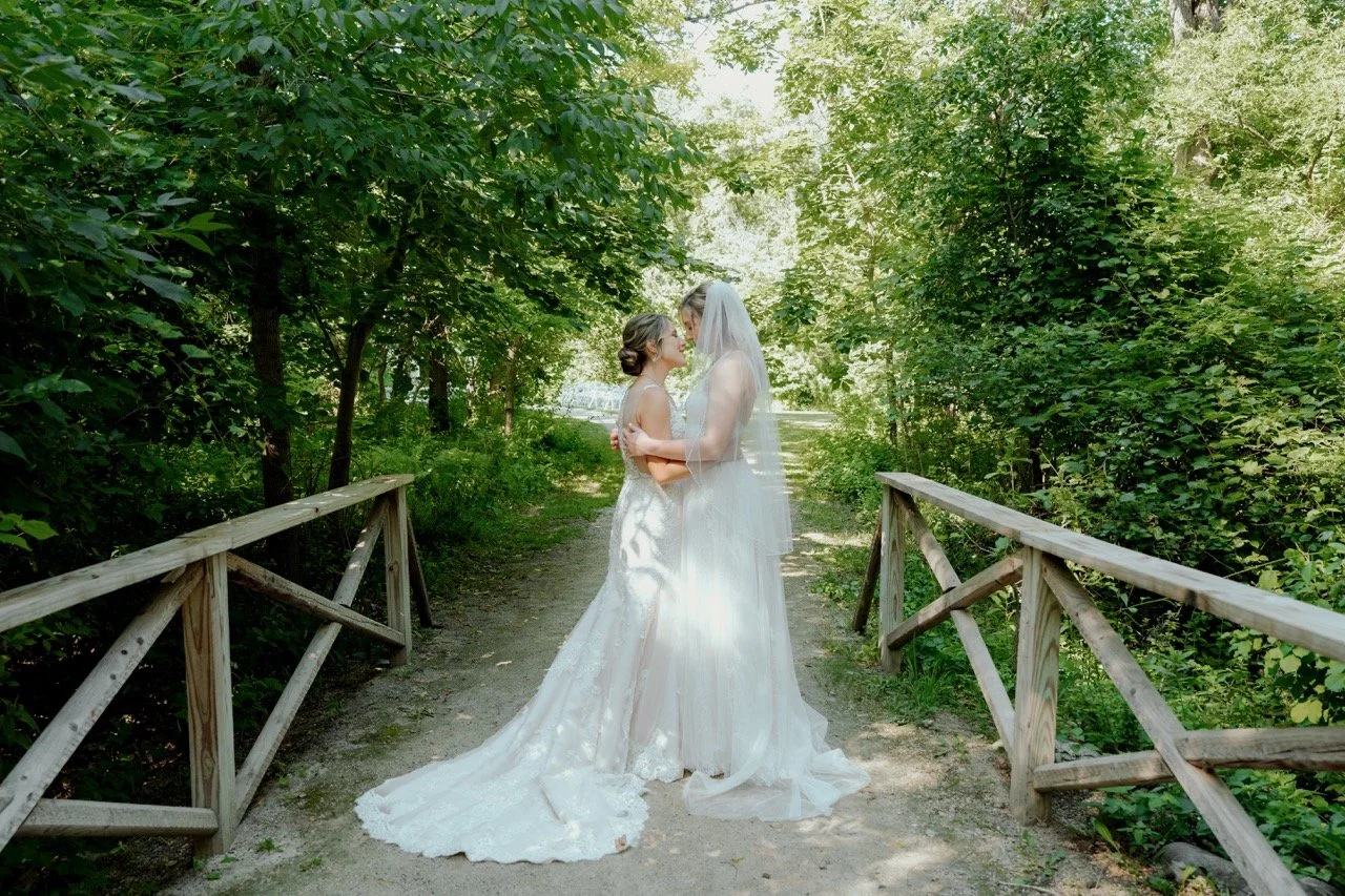 Two brides holding each other on paved bridge outdoors