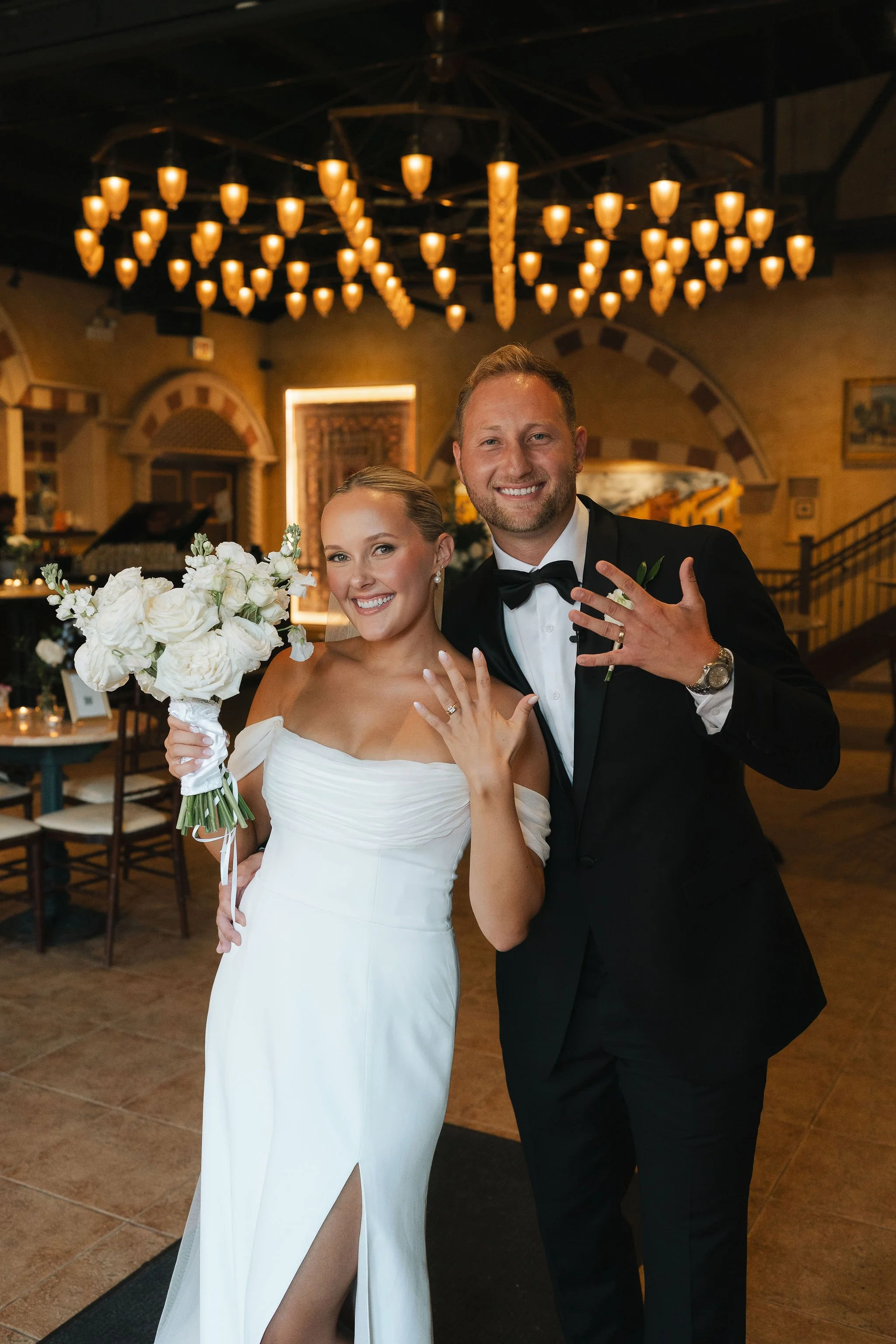 bride and groom standing next to each other holding up their hands to show off their rings with Italian style venue in the background