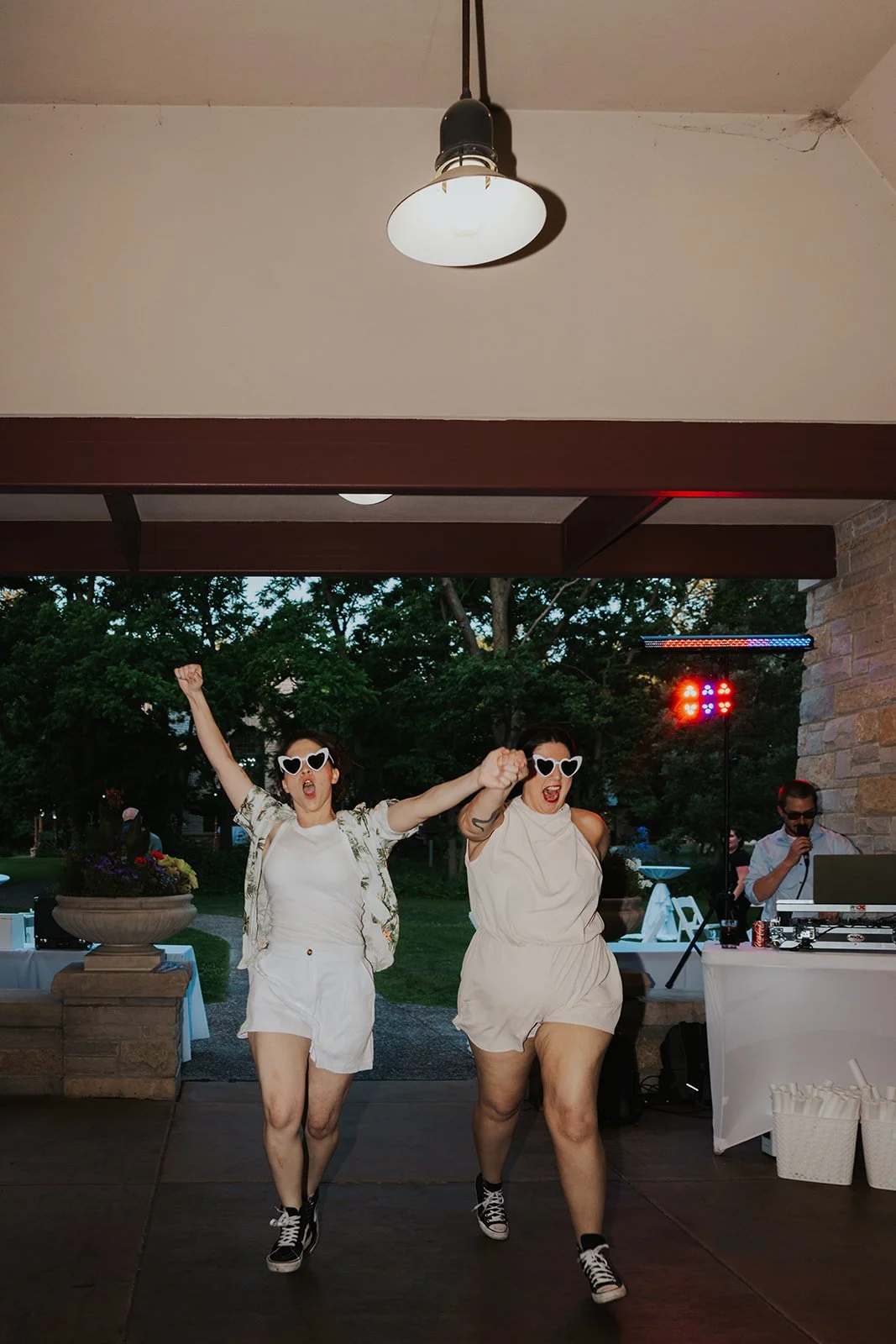 Two brides in new reception outfits holding hands up and cheering entering pavilion