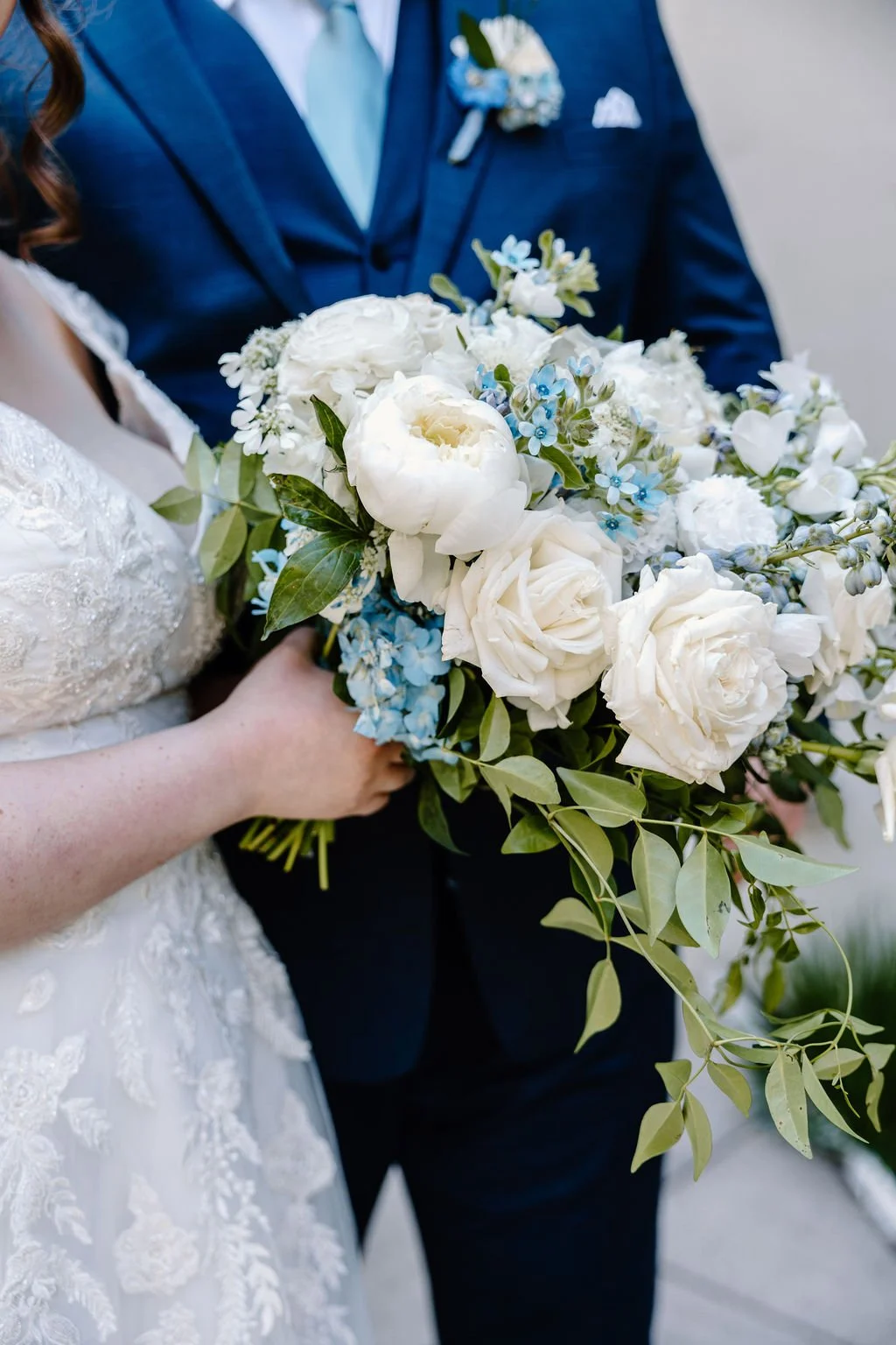 White and blue flowers for bridal bouquet close up with bride holding it near groom