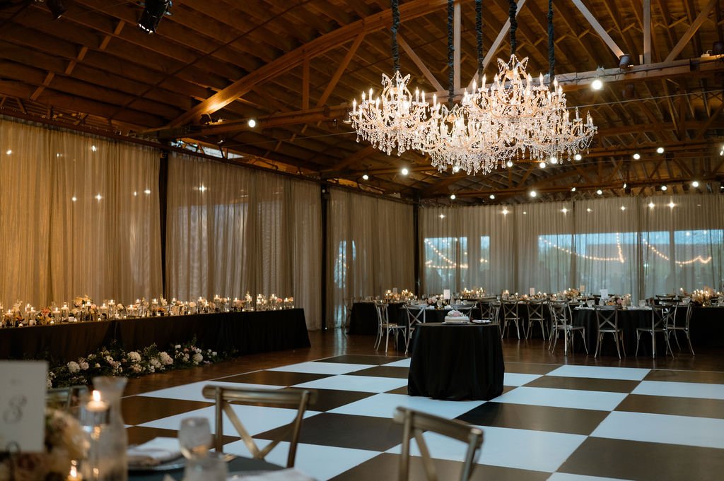 modern black and white checkered dance floor with group of chandeliers above and black linen tables with candles