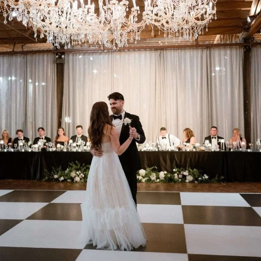 Chicago couple doing first dance on checkered black and white dance floor with wedding party sitting behind them