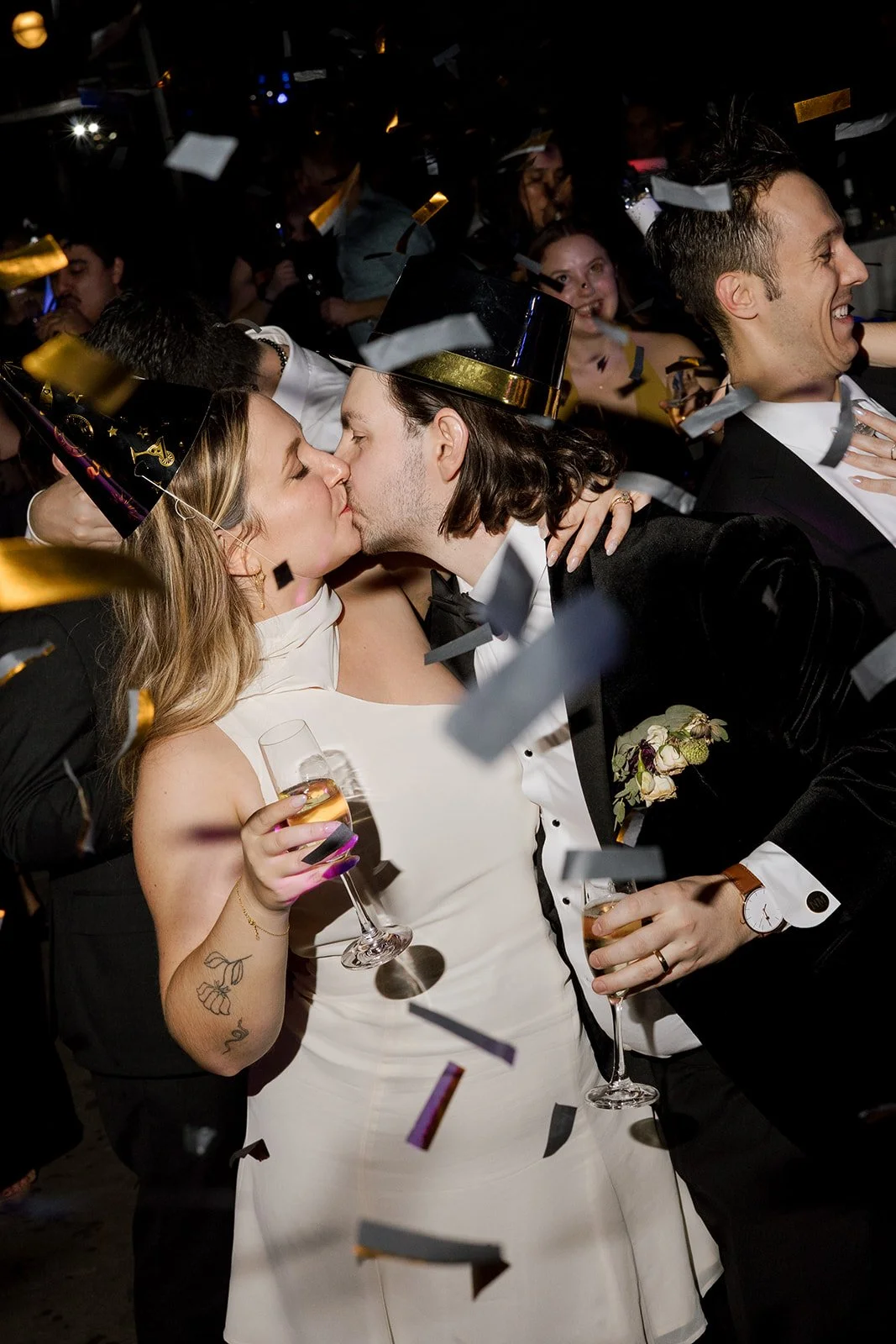 Bride and groom kiss with confetti at NYE Midnight holding champagne and wedding guests smiling